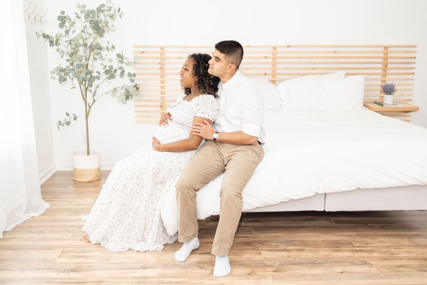 A couple in wedding attire embraces while dancing in a bright studio space with wooden floors and white walls.