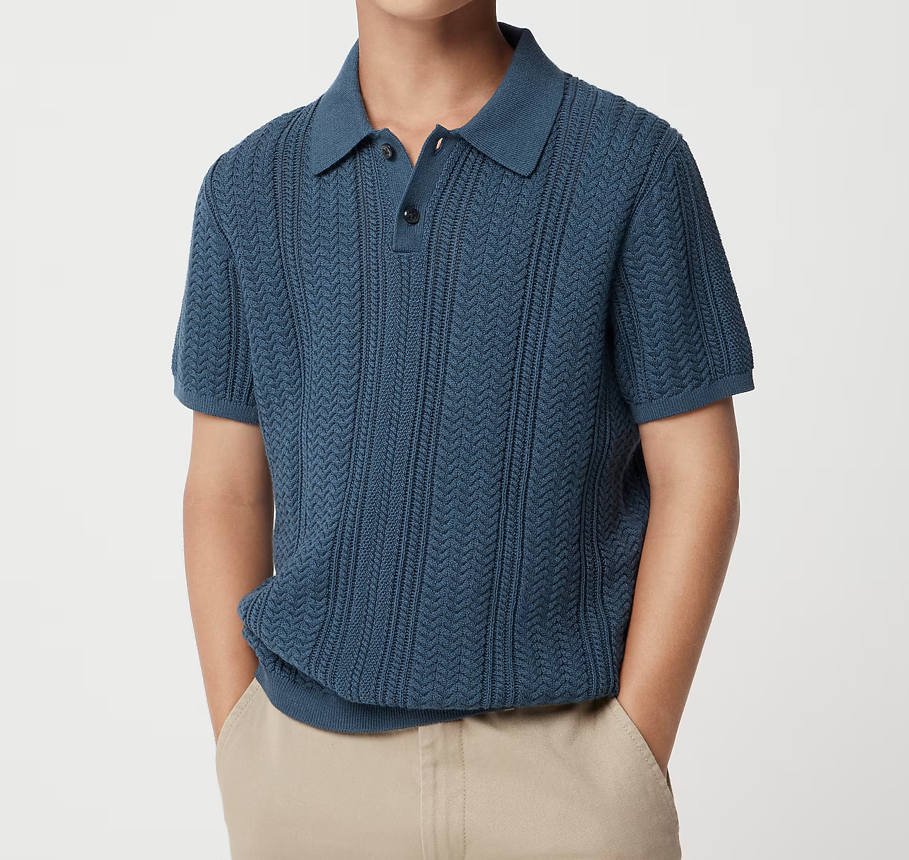 Man wearing a blue textured knit polo shirt with short sleeves and button placket, paired with beige chinos.