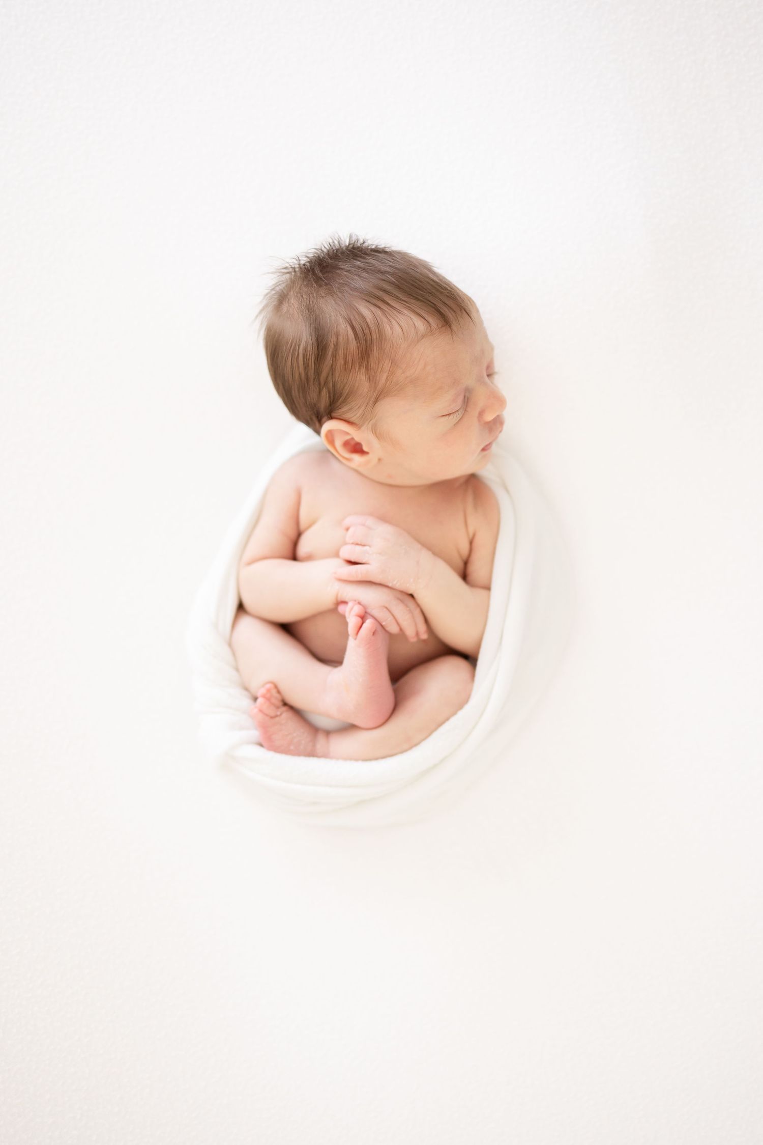 Sleeping newborn baby curled up peacefully in white wrap during luxury newborn photography session in Columbus, GA