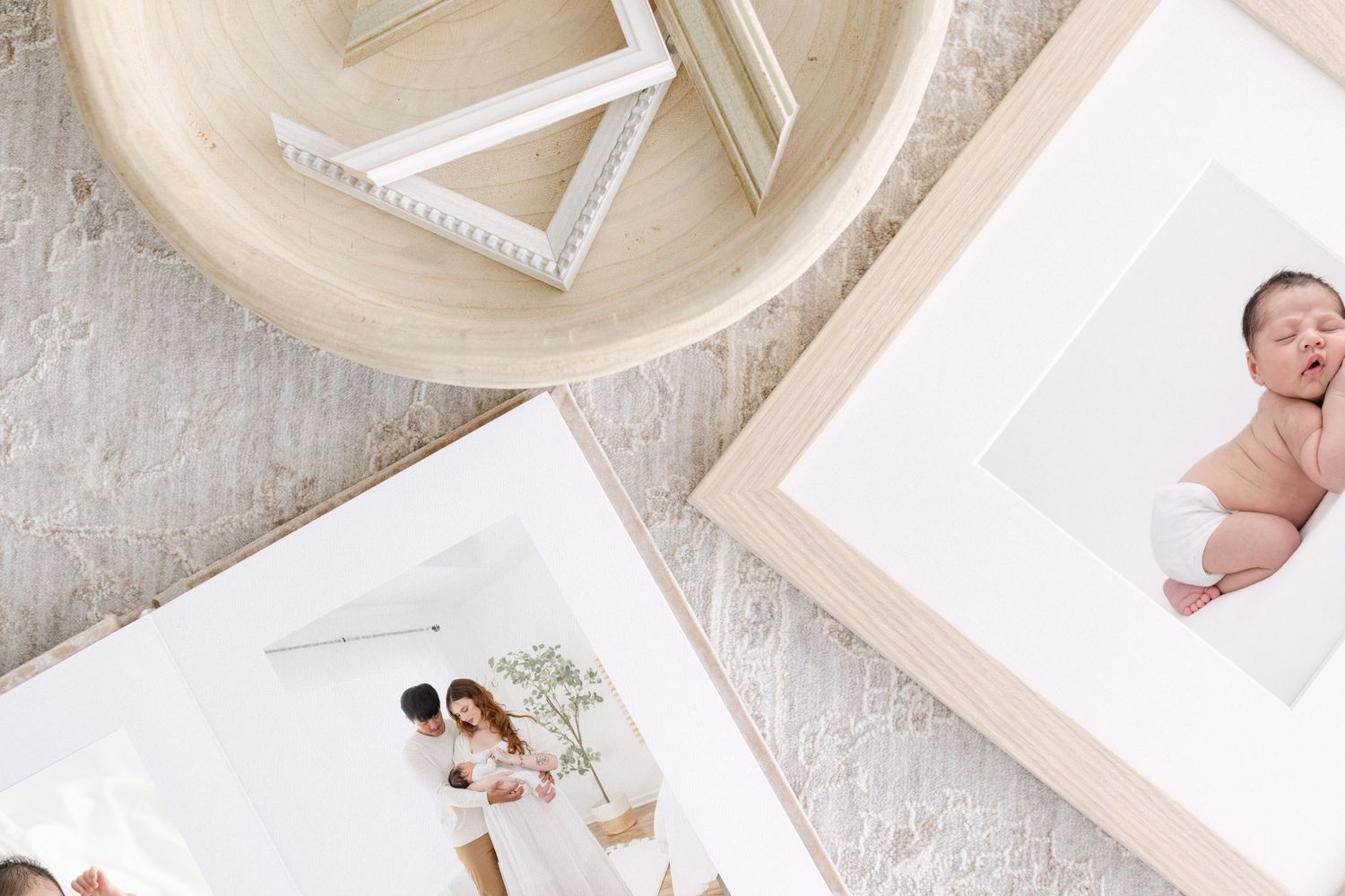 Framed maternity and family photos displayed on a soft rug beside a wooden tray with white picture frames.