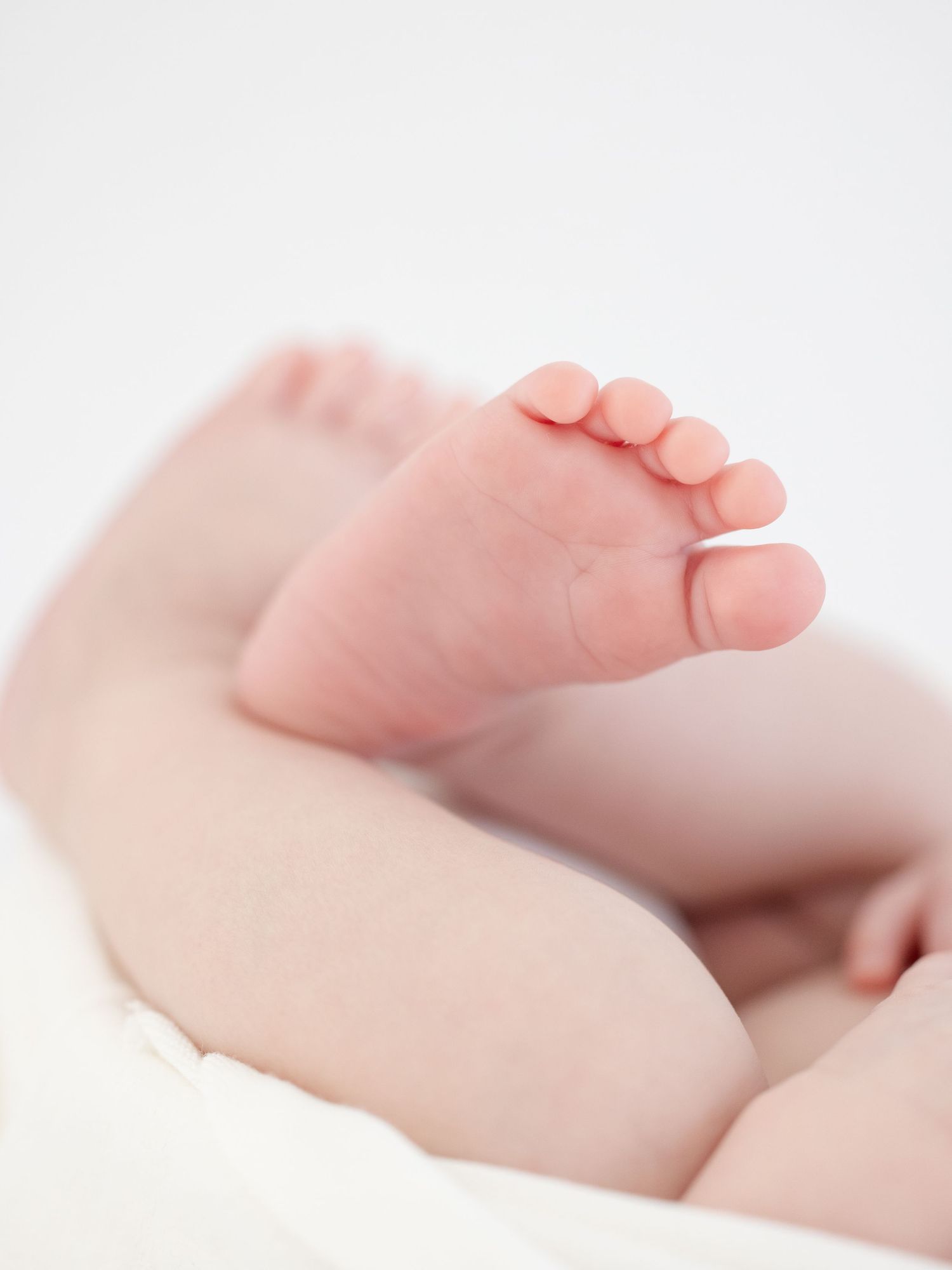 Close-up of tiny newborn baby feet with delicate toes against soft white background by newborn photographer in Columbus, GA.
