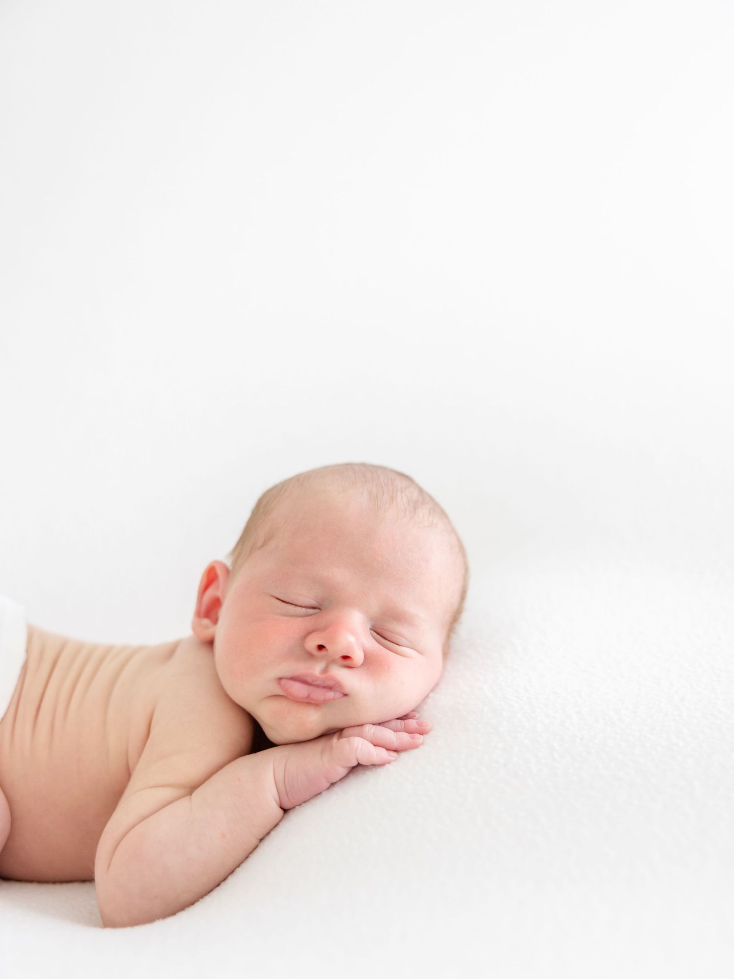 A sleeping newborn baby in a peaceful pose against a white background by luxury Columbus, GA newborn photographer.