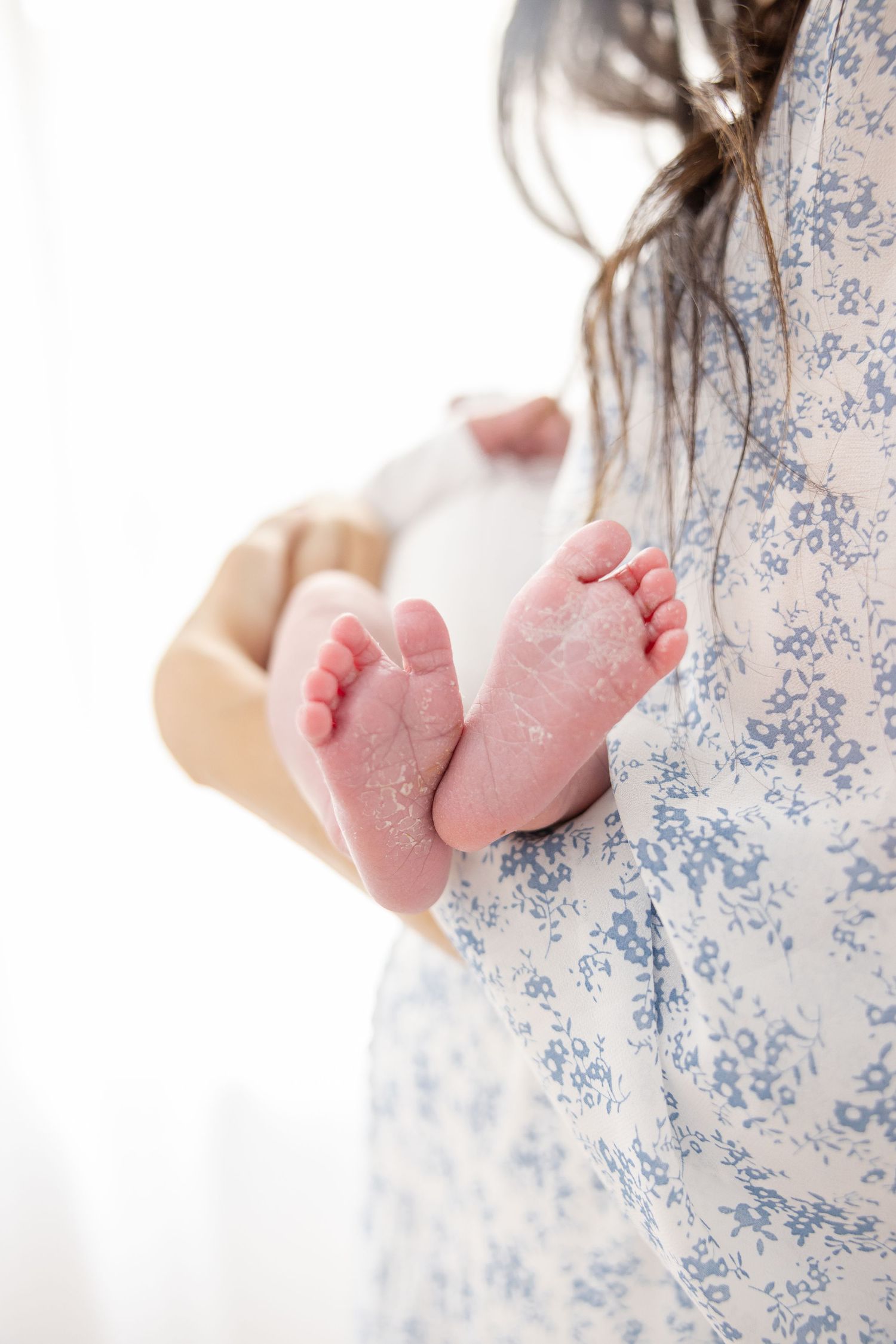 Close up of tiny newborn feet against blue floral dress fabric in soft light at Columbus, GA newborn photography session.