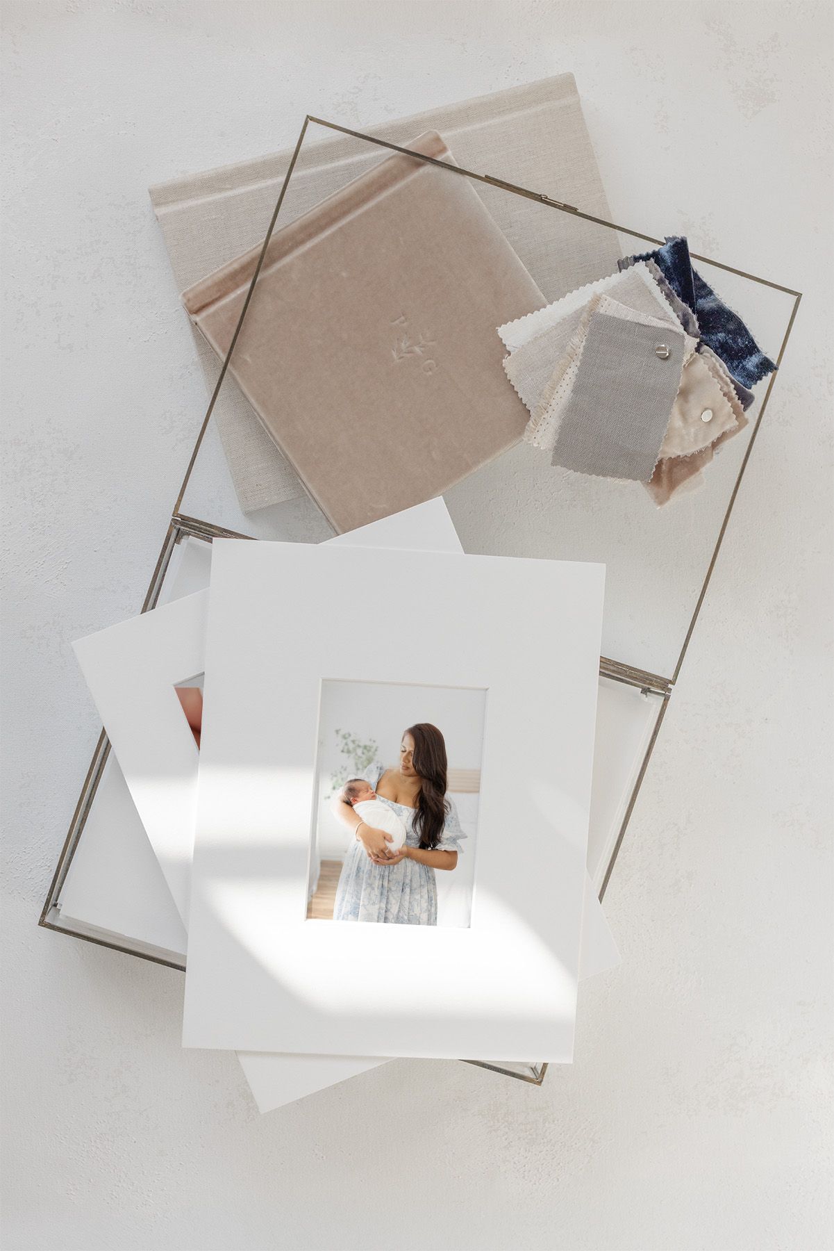 Flat lay of matted photos and fabric sample books in neutral tones arranged in a metal frame on white surface.