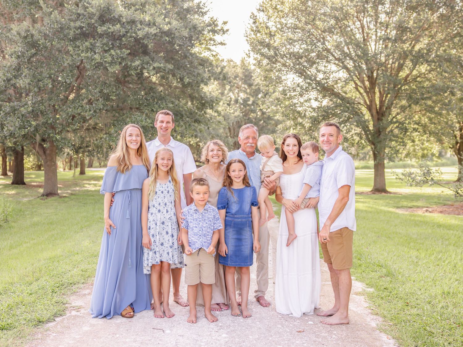 A group of people wearing coordinated blue and white outfits pose together on a grassy hill during golden hour.