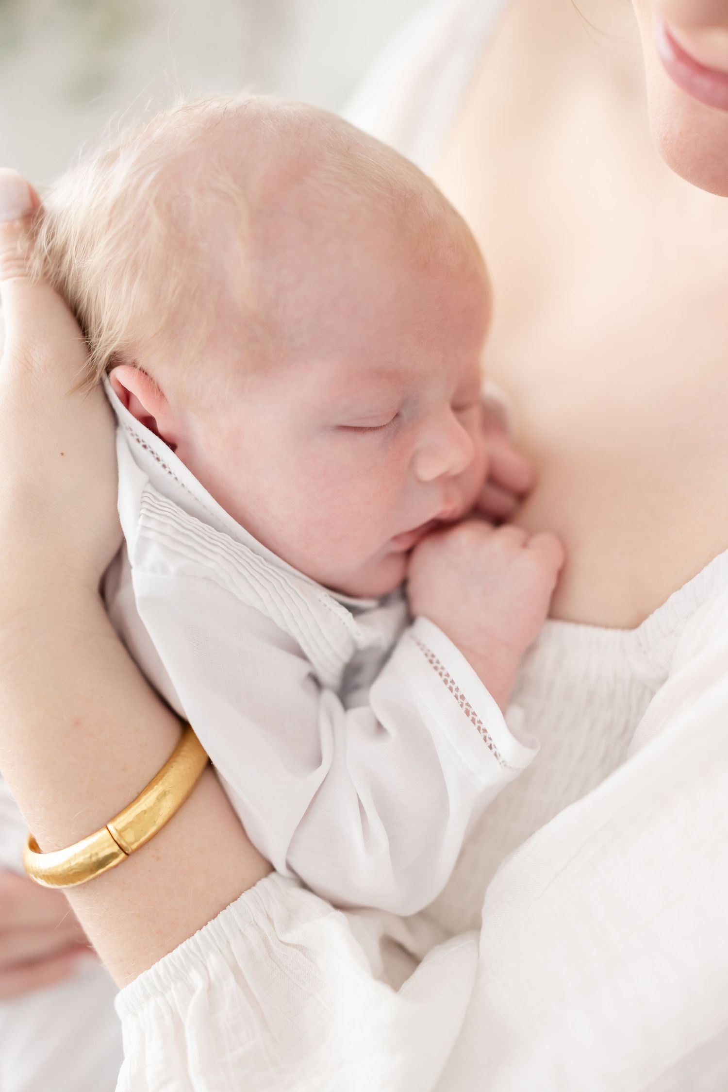 A newborn baby in white clothing sleeps against mom’s chest at his Columbus, GA studio newborn session.