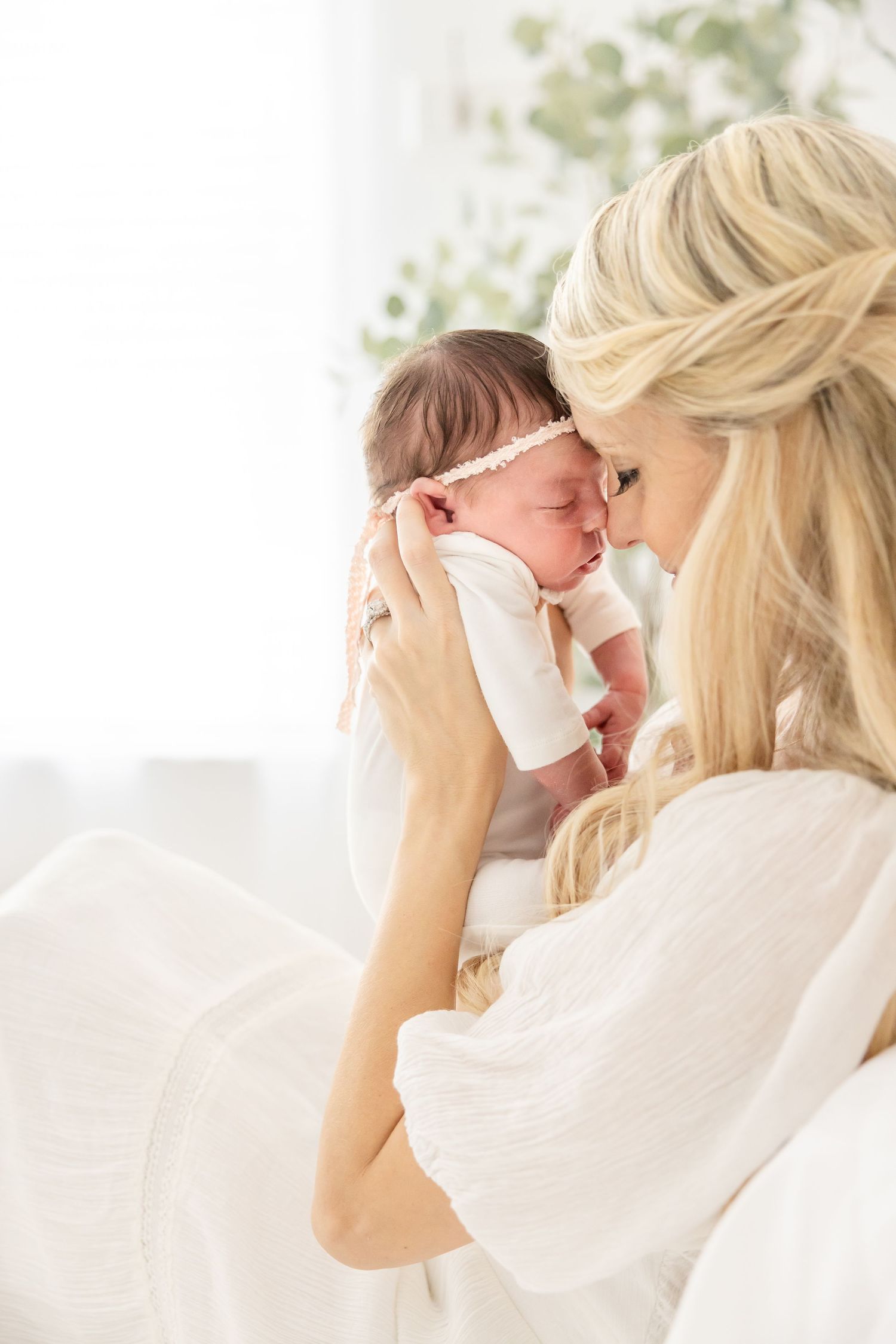 Mother in white holding newborn baby in tender intimate moment against bright window at their Columbus, GA newborn photography session.