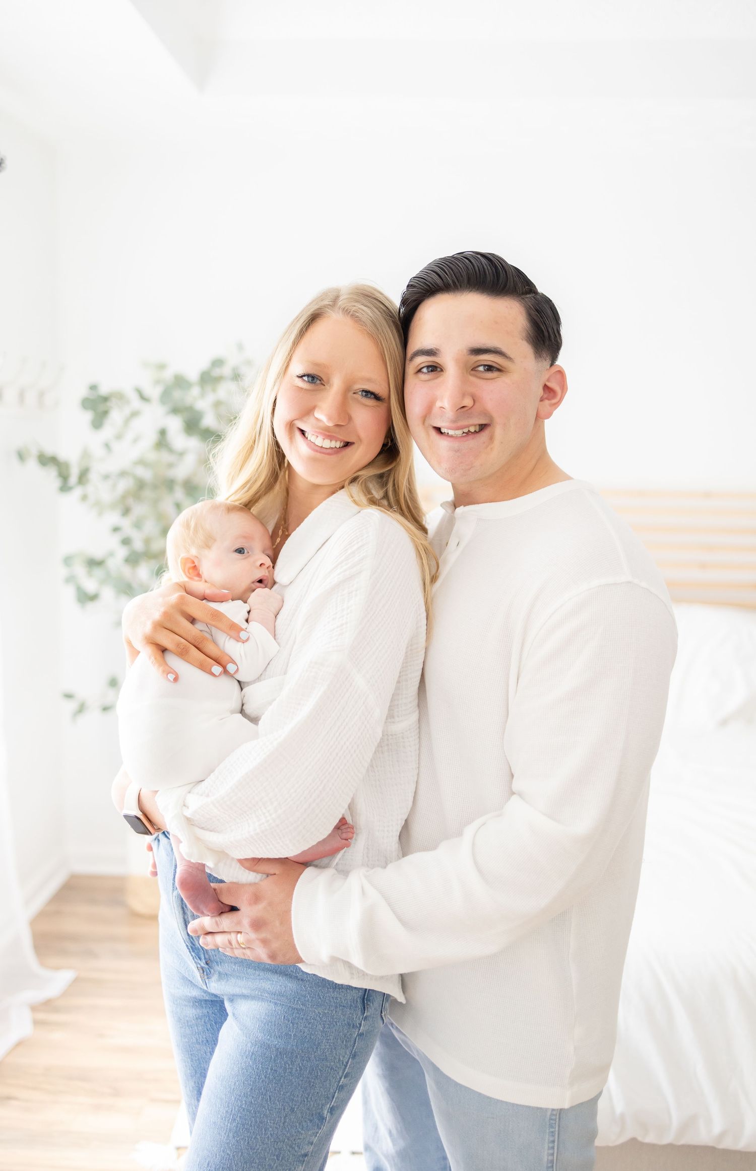 Portrait of new parents in white shirts and jeans holding their 6 week old baby at their Columbus, GA newborn photography session.