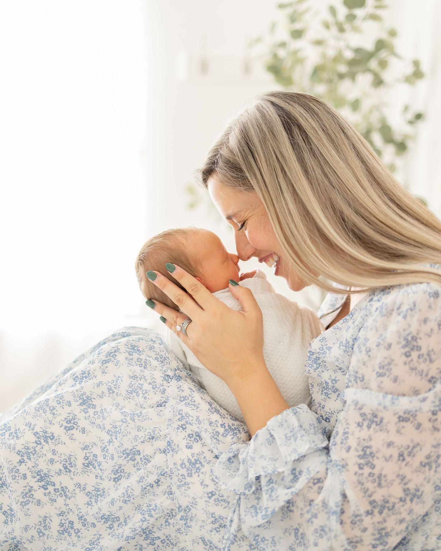 A tender moment between mother and newborn baby in a blue floral dress against a light background by Columbus, GA Newborn Photographer.