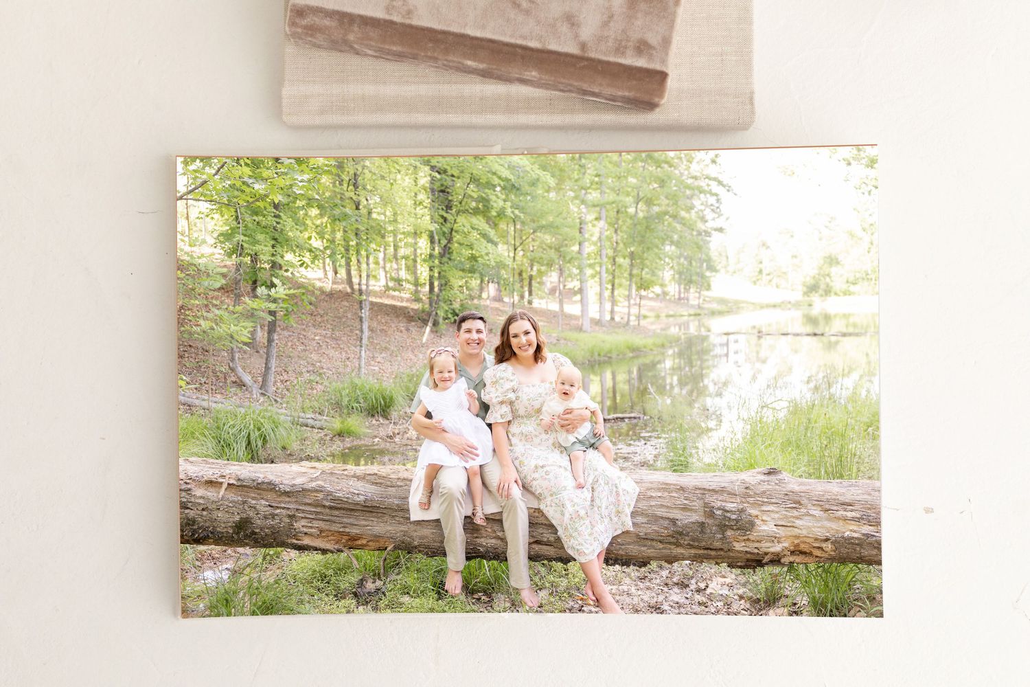 Family of four sitting on a fallen log outdoors near a pond, printed in a professional heirloom album by Columbus, GA family photographer.