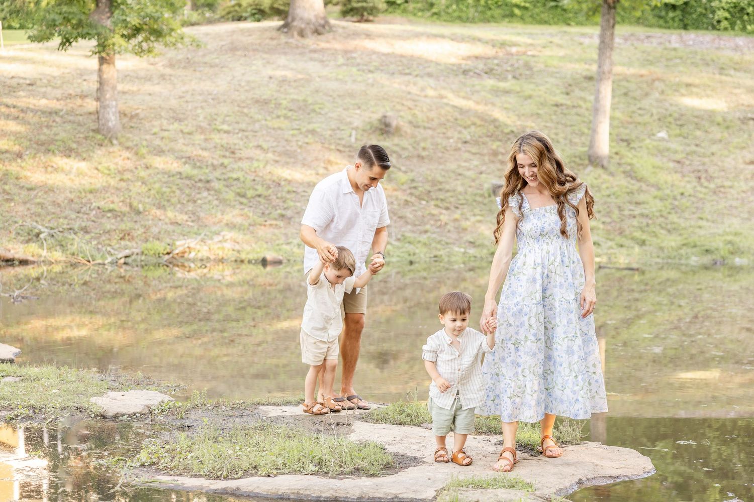 Four people enjoying a sunny afternoon together by a pond in a peaceful park setting.