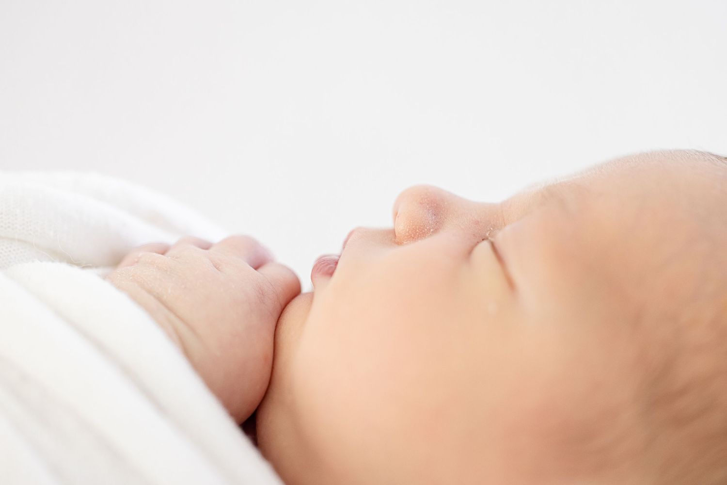 Peaceful sleeping baby wrapped in soft white blanket lying on light background showing gentle profile.