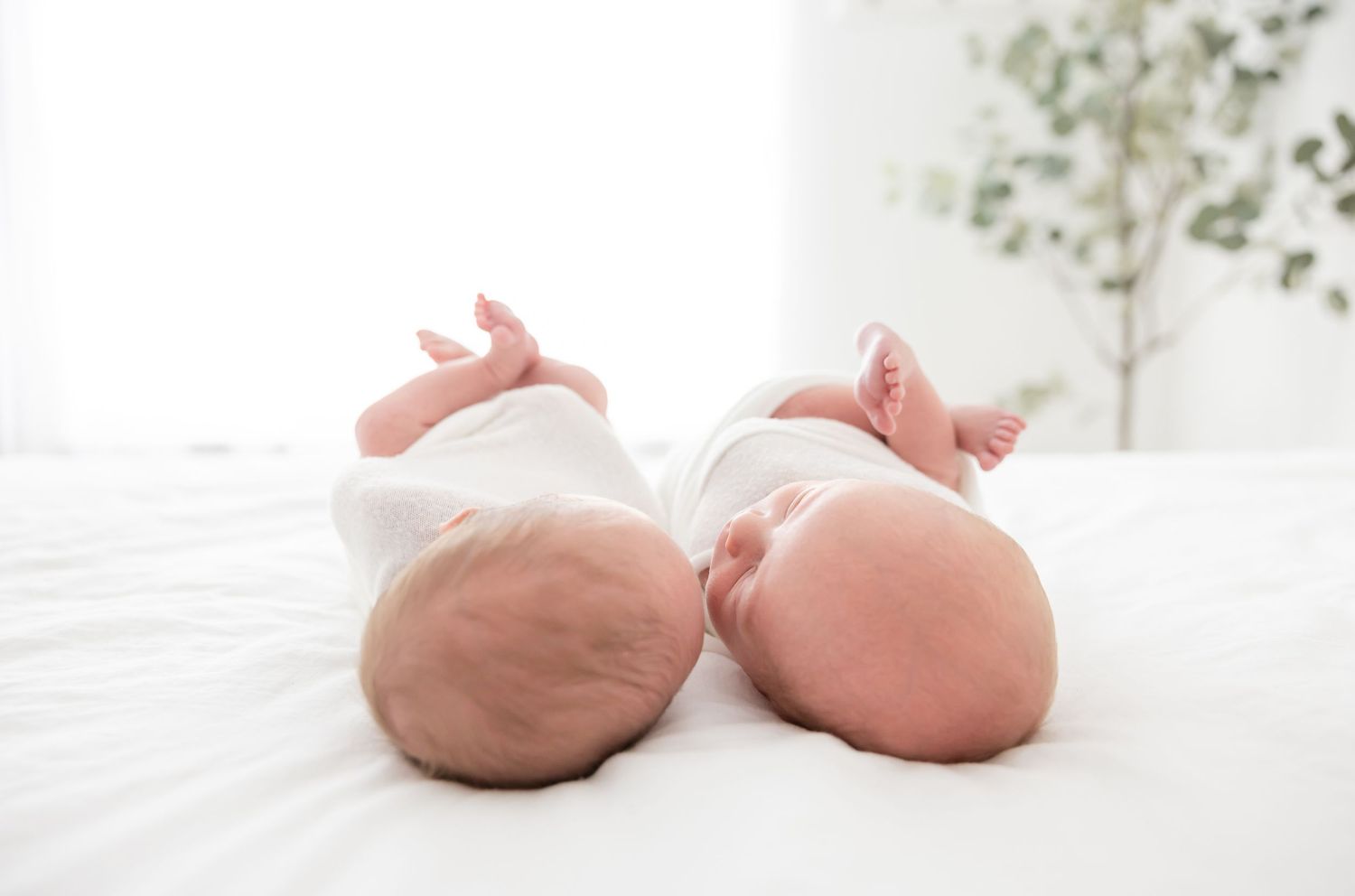 Twin newborns lay on a soft white bed at their Columbus, GA newborn portrait session.