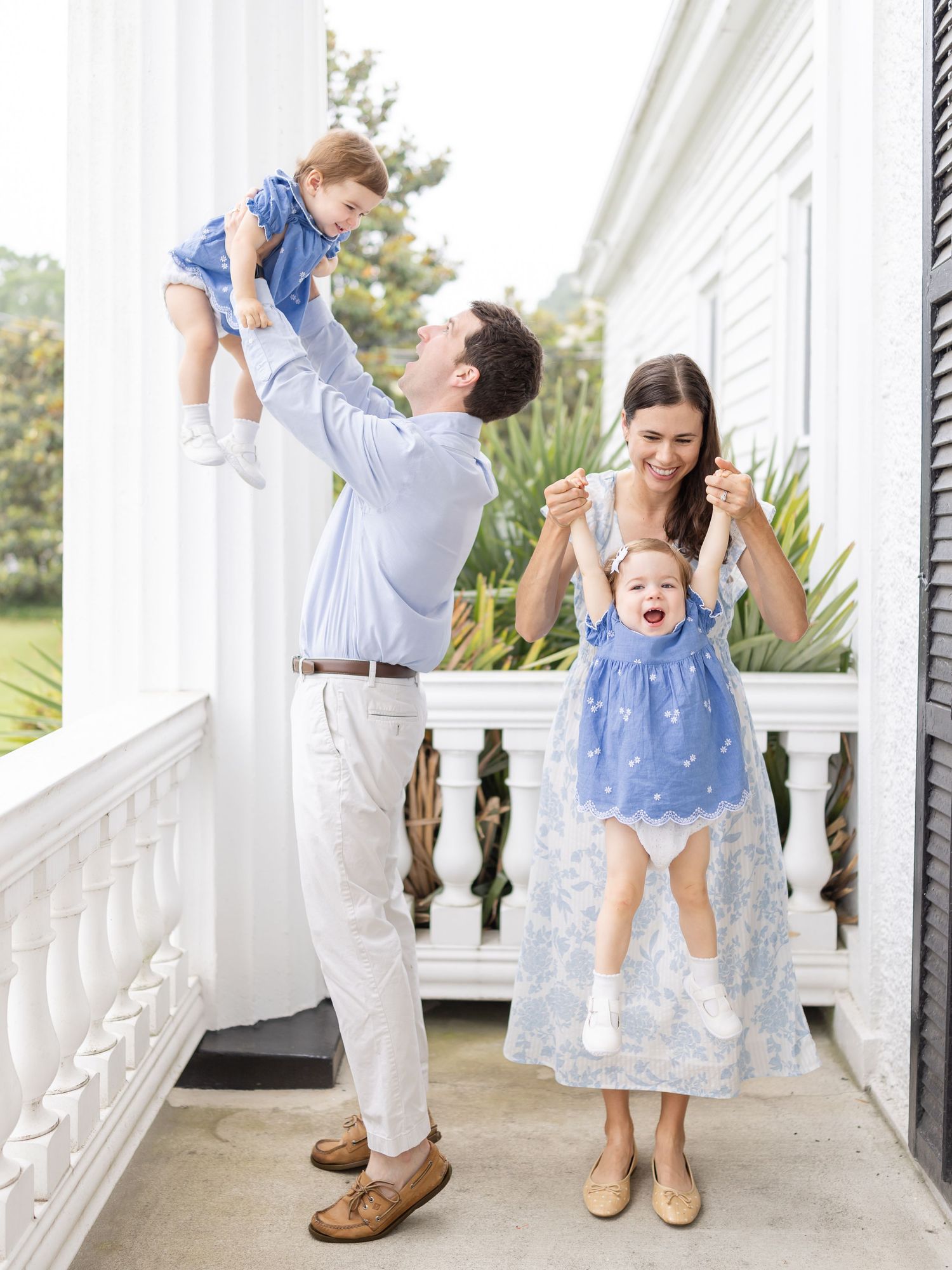 A parent and child share a tender moment on a white porch while dressed in coordinating blue and white outfits.