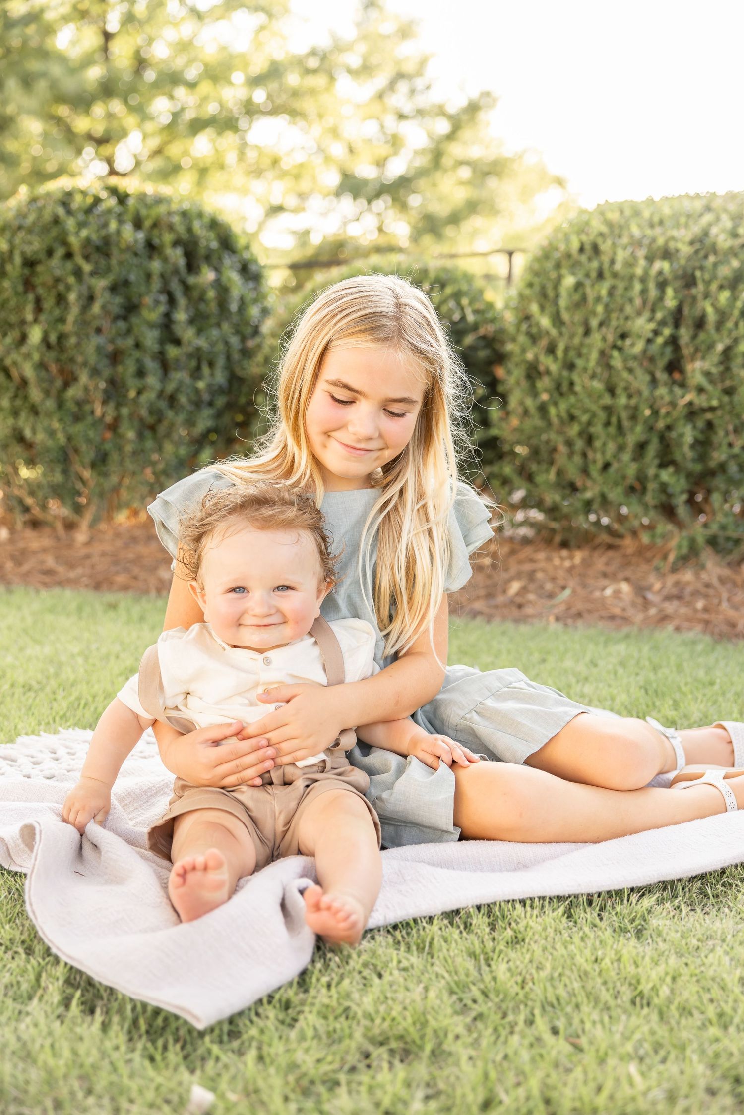 Siblings sitting on a blanket in the grass hugging during their family summer portraits in Columbus, GA.