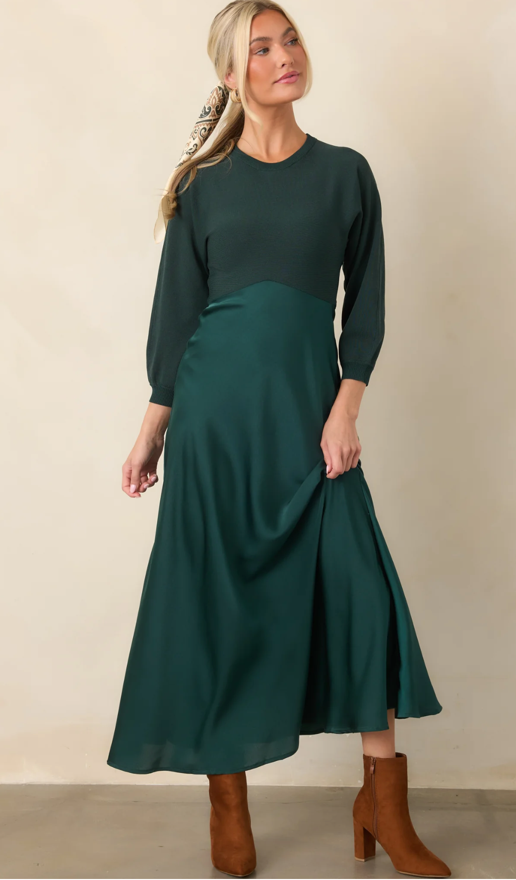 Woman wearing an emerald green midi dress with 3/4 sleeves and satin skirt, paired with tan block heel boots.