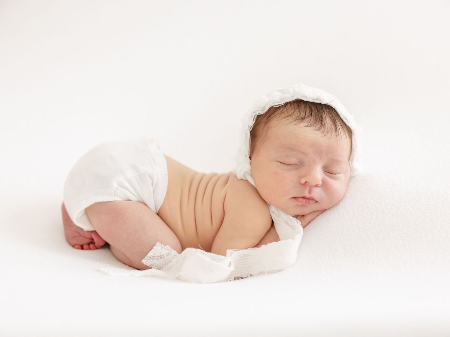 Peaceful sleeping baby with a white lace bonnet sleeping peacefully during her Columbus, GA newborn photography session.