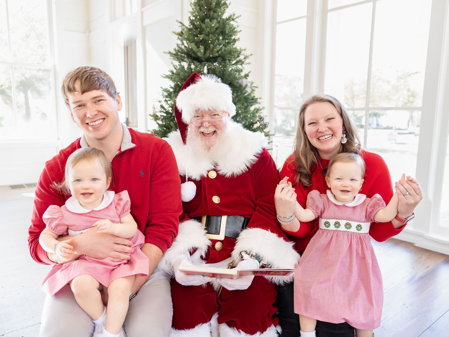 Family with two toddlers posing with Santa Claus in front of a Christmas tree during holiday photo session.
