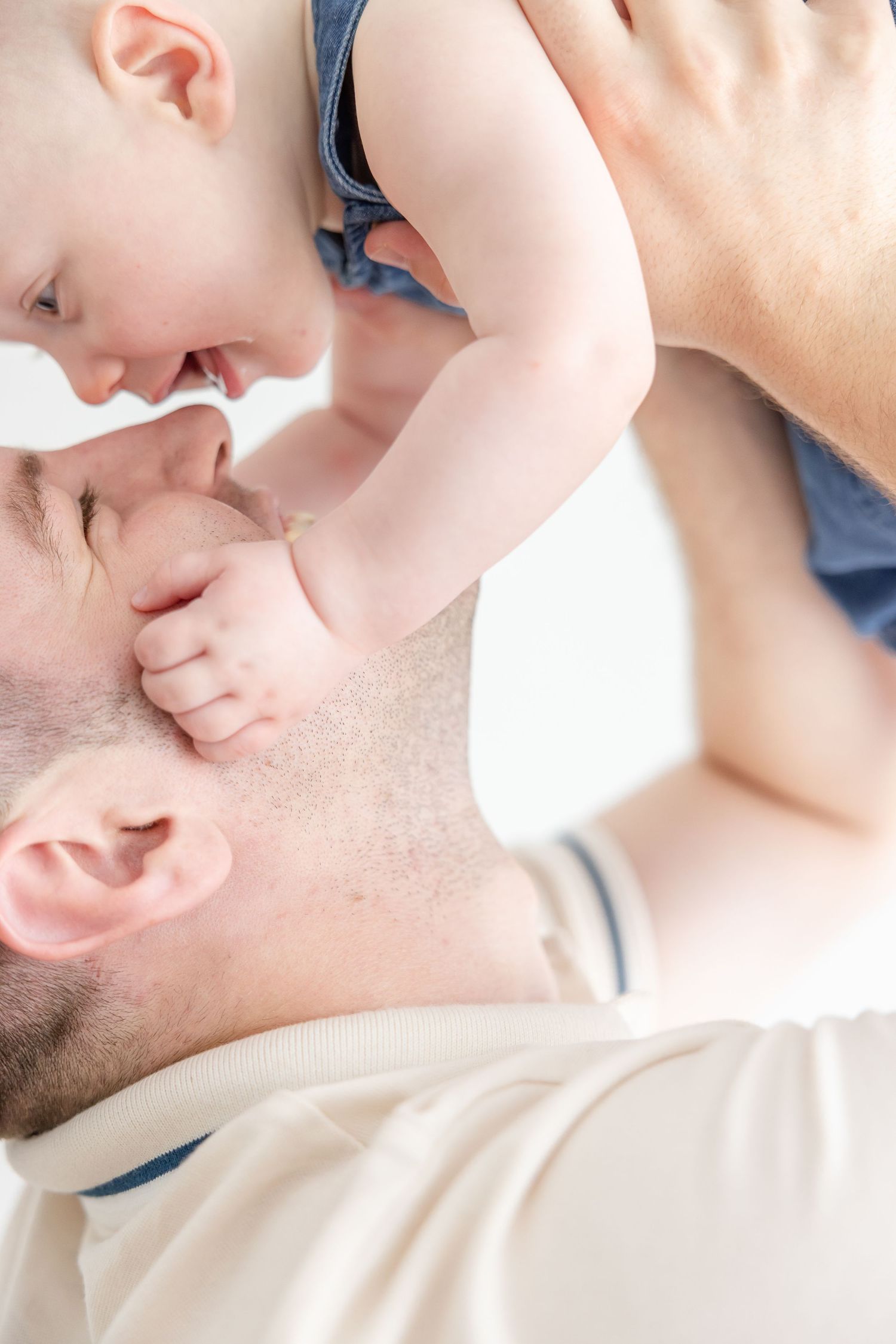 A father lovingly holds his baby close, touching noses in a tender moment of bonding on a white background.