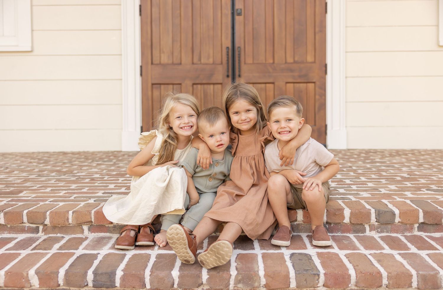 Four siblings sit on brick stairs with their arms wrapped around each other smiling at the camera for family photos in Columbus, GA.