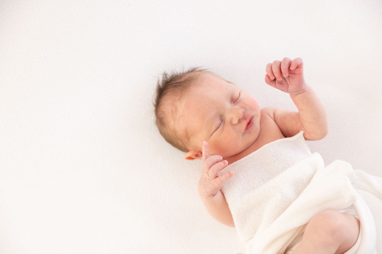 Newborn baby sleeping peacefully in soft white bedding with natural lighting at her studio newborn session in Columbus, GA.