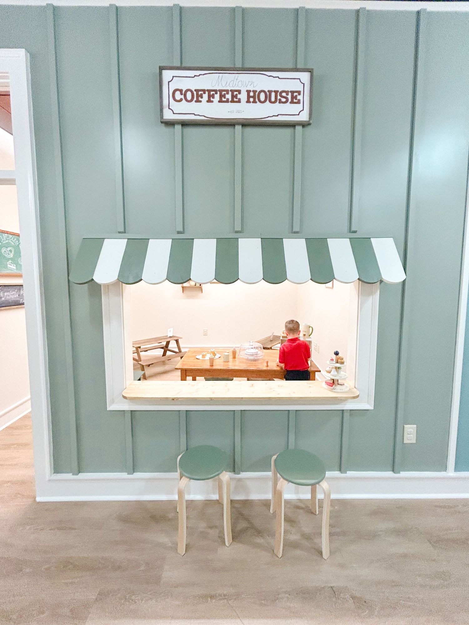 A miniature coffee house storefront display with a striped awning and small wooden furniture creates a charming cafe scene.