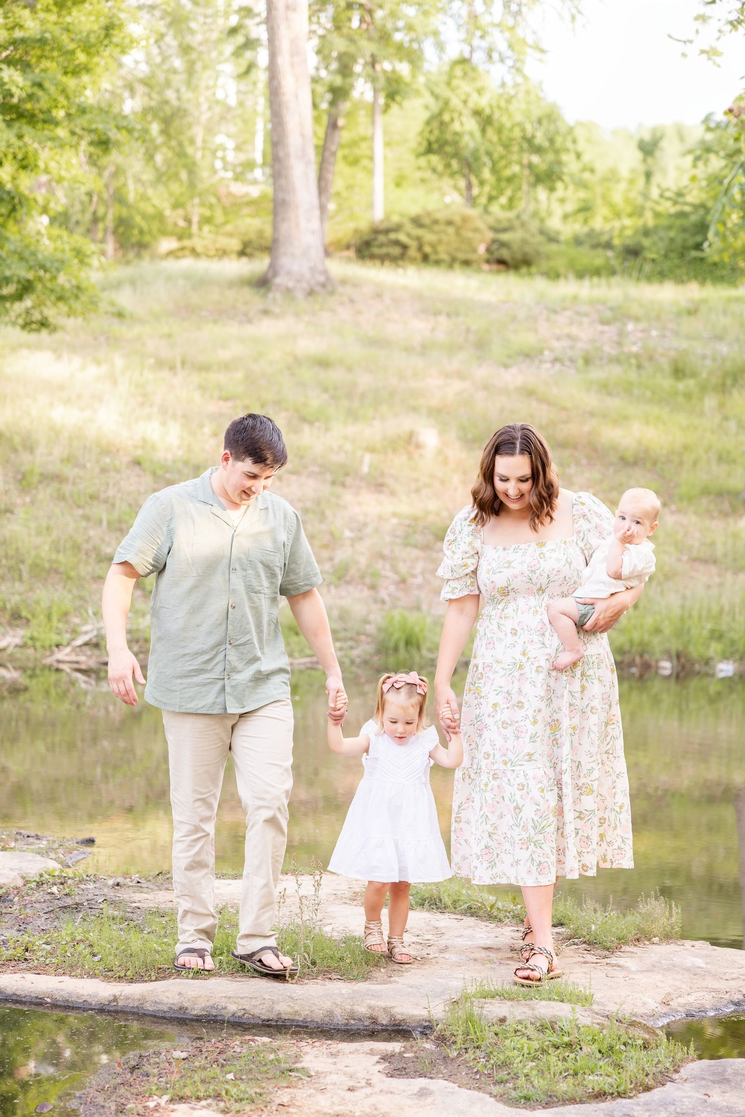 Family of four walking outdoors during spring in Columbus, GA wearing pastel outfits near a pond by Columbus, GA family photographer.