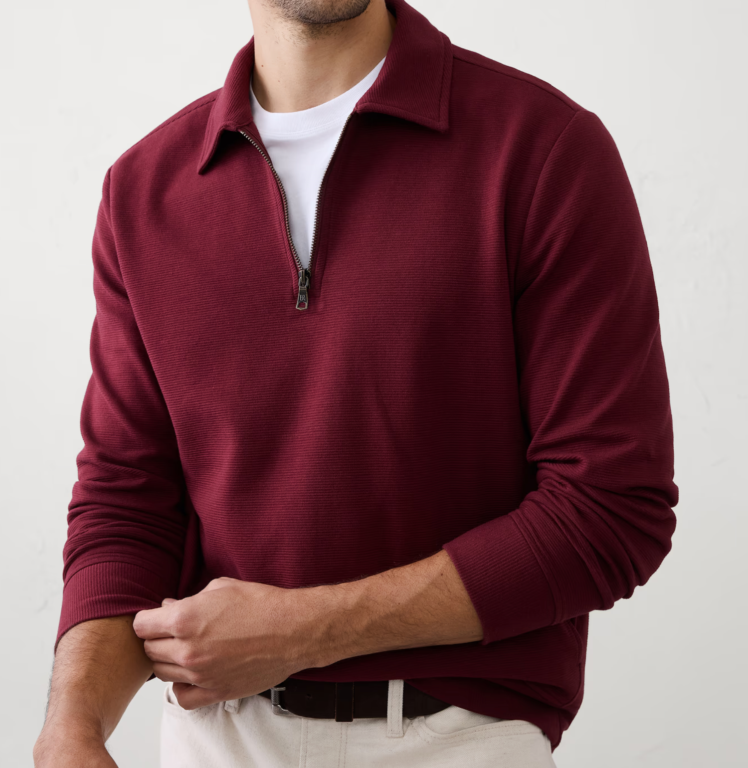 Man wearing a burgundy quarter-zip pullover sweater with collar over a white t-shirt and khaki pants.