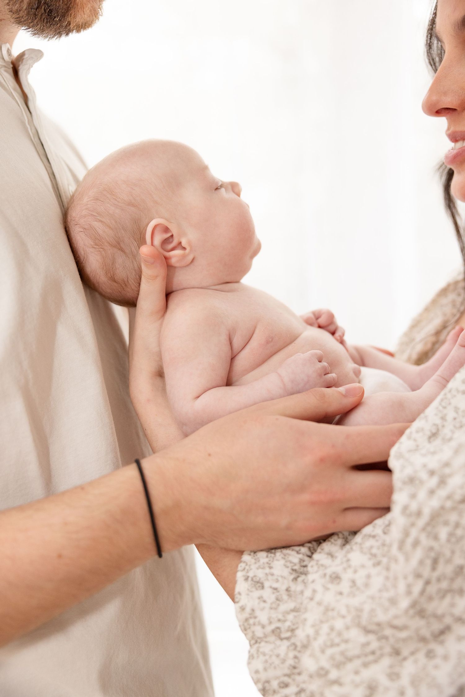 A newborn baby held tenderly between parents in soft natural light against a white background.