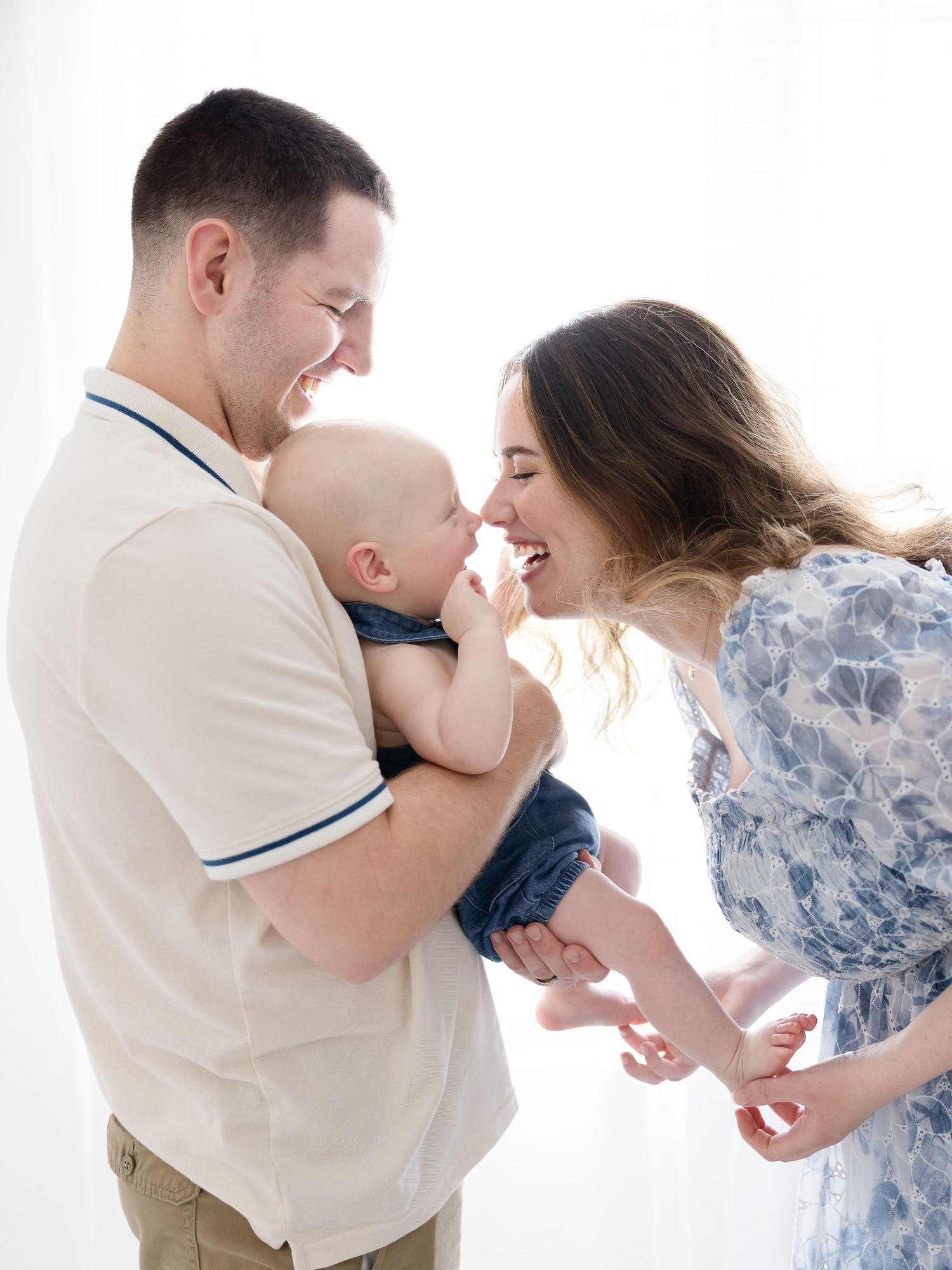 Happy young family with mother and father smiling at their baby boy in a bright white studio setting.