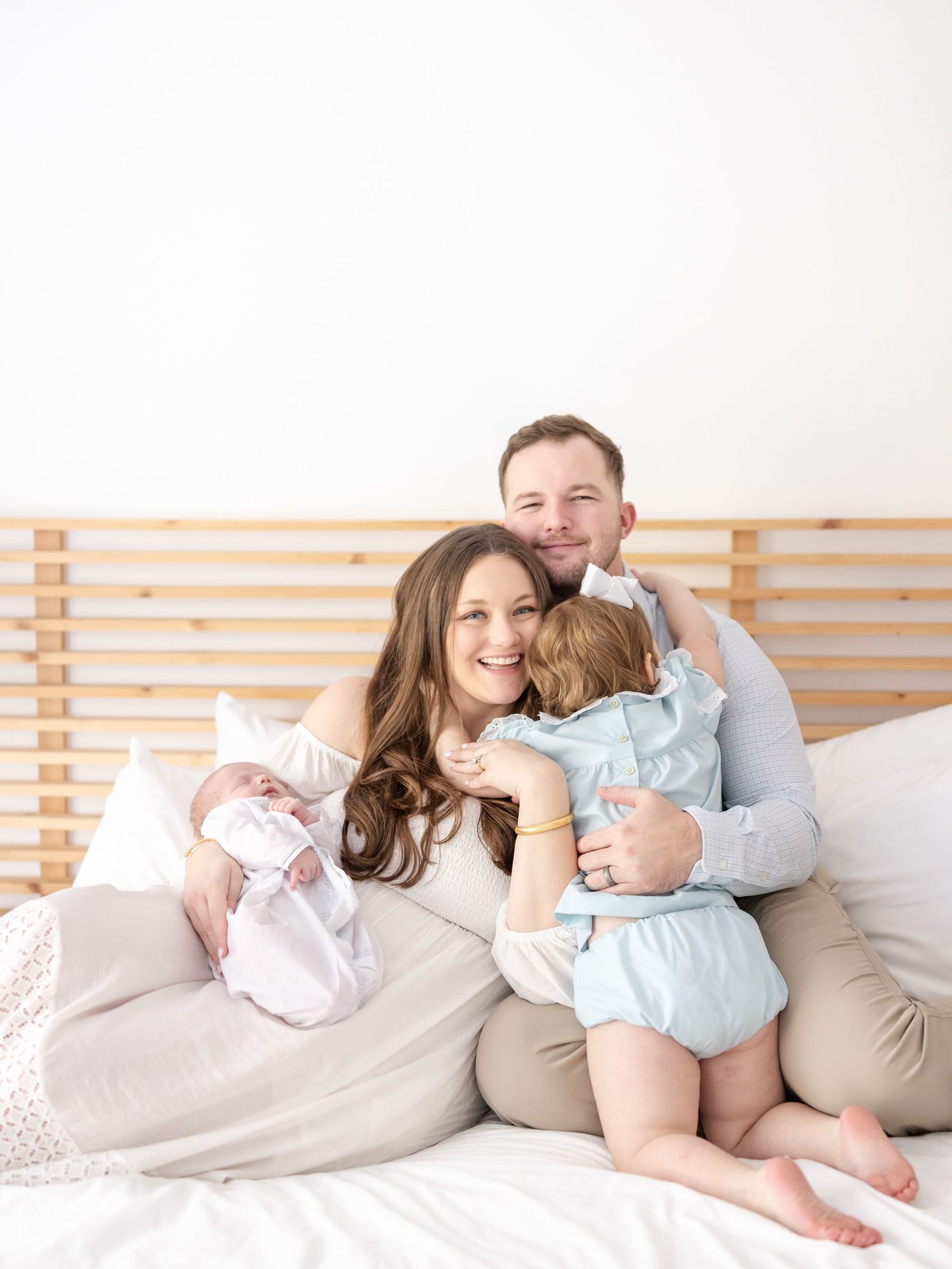 Family relaxing together on cozy white bedding while sharing a family hug during in-studio Columbus GA newborn session.