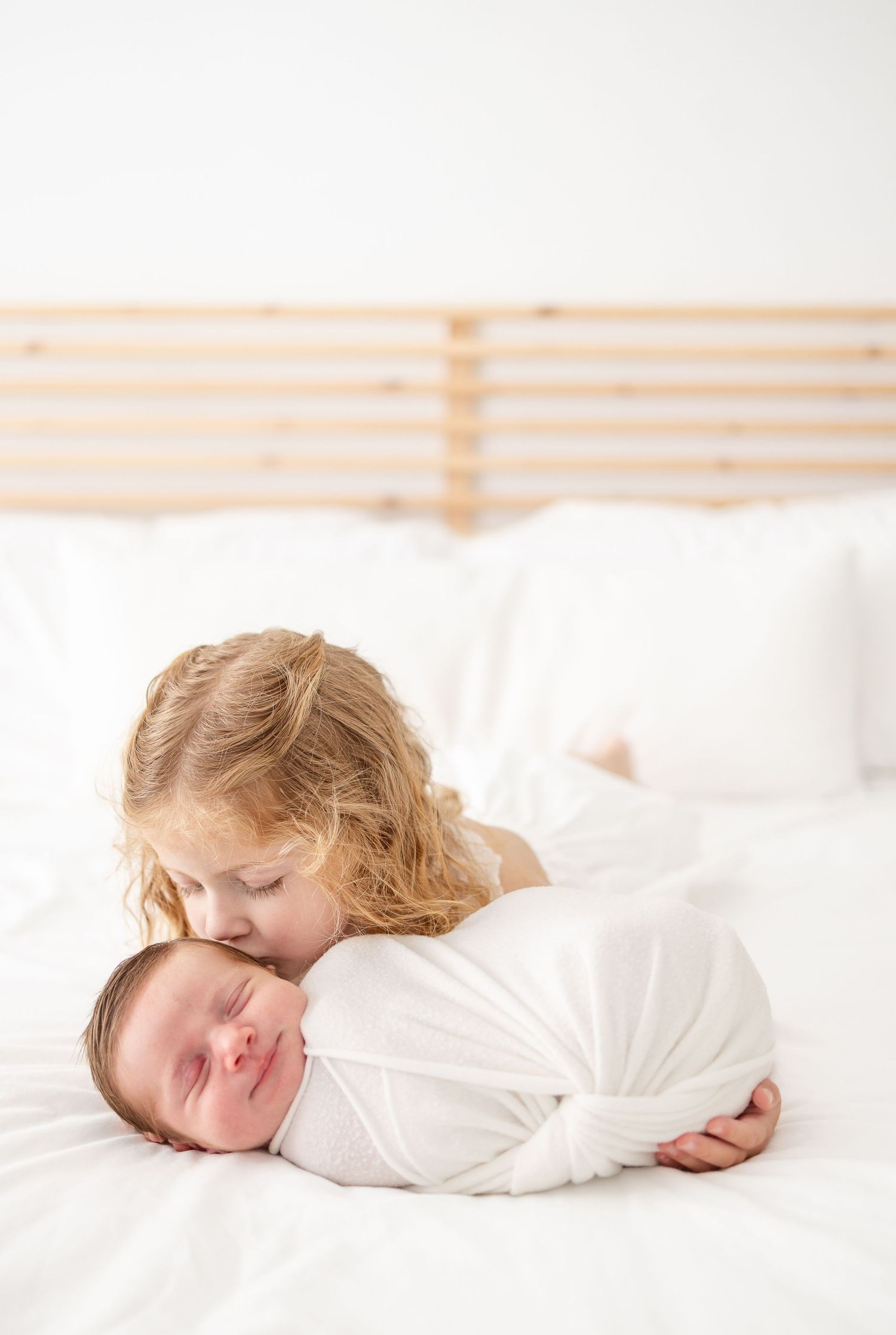 Little girl with red hair holds her newborn brother and gives him a kiss during Columbus, GA newborn studio portrait session.