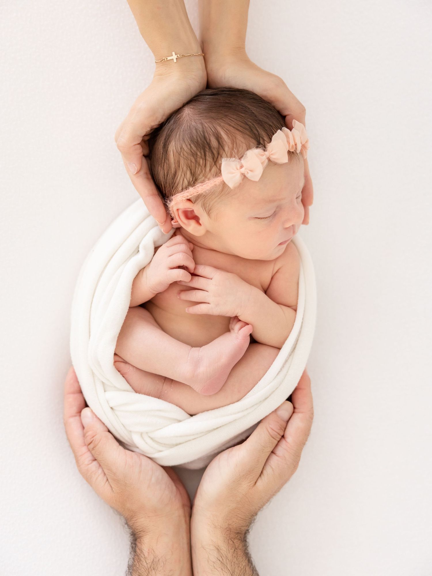 Newborn baby sleeping peacefully in parents' hands wrapped in white fabric during an in-studio newborn session in Columbus, GA.