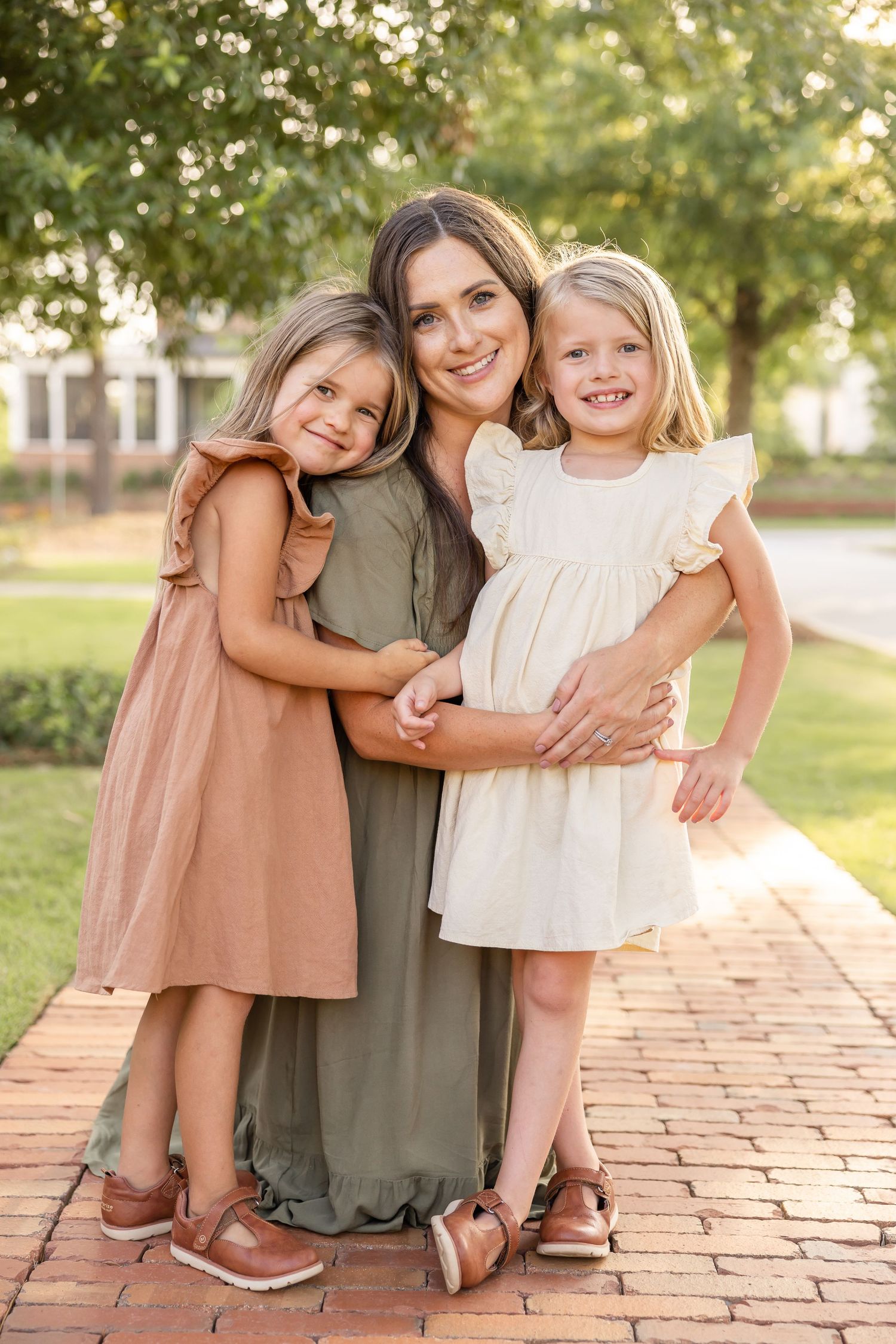 A kneeling on brick pavement snuggles her two girls at family photos in Columbus, GA.
