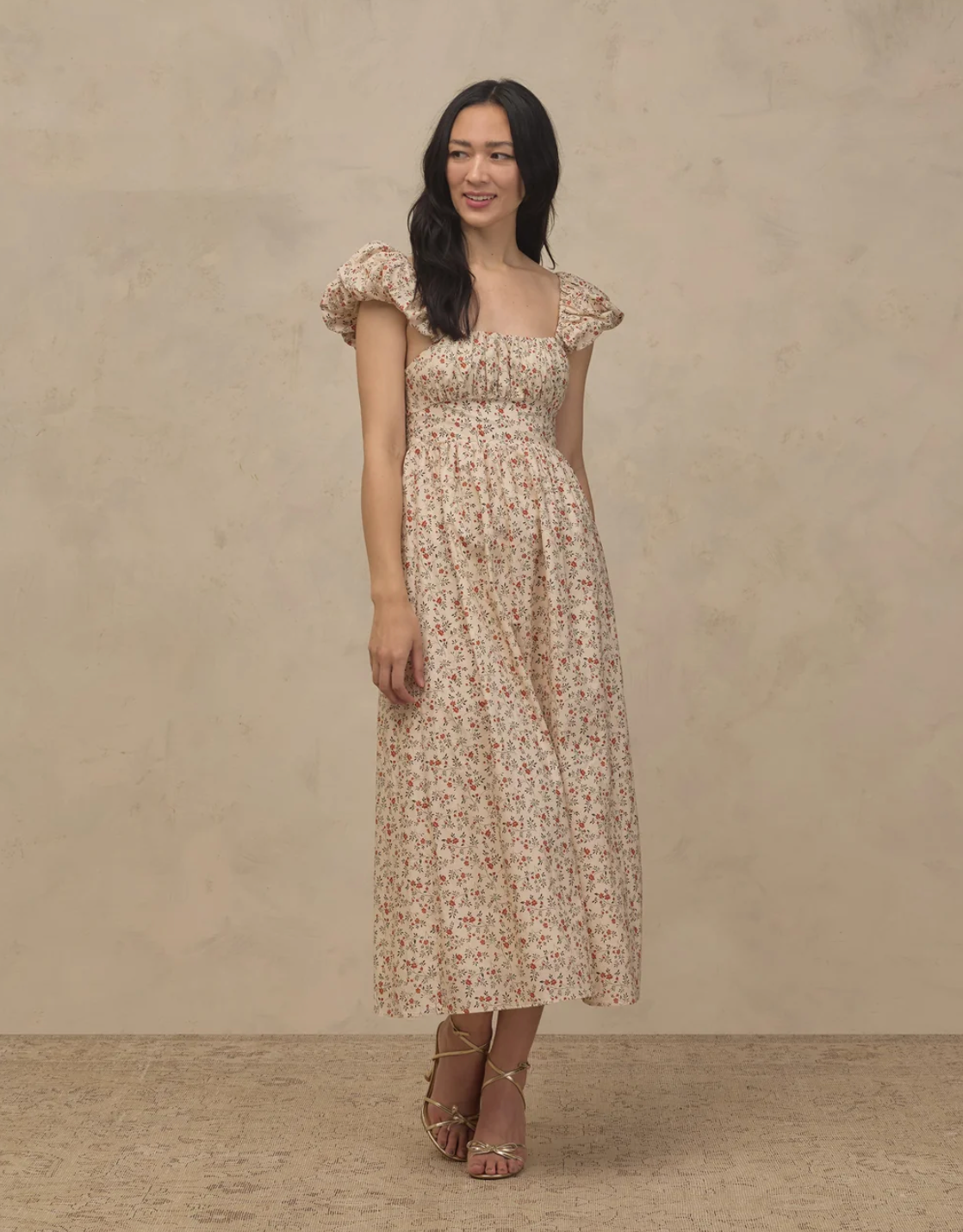 Woman wearing a floral midi dress with puff sleeves, smocked bodice, and tiered skirt in cream and pink tones.