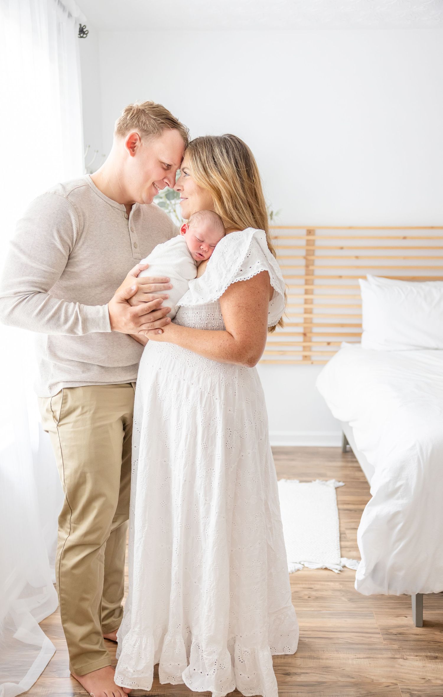 Couple in white and beige clothing share quiet moment together with their newborn in a bright minimalist room with Columbus GA photographer