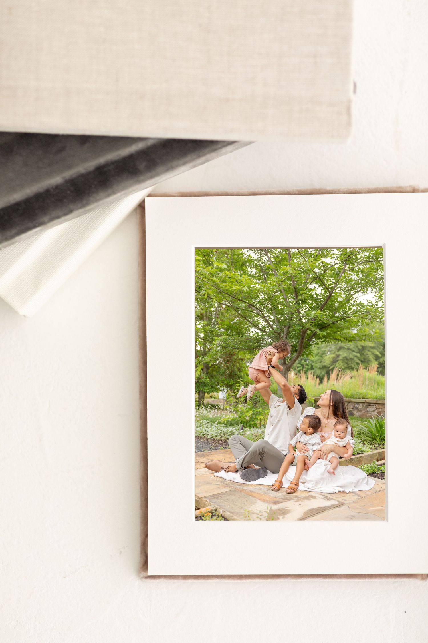 A matted family photo album displayed against a white backdrop, showing parents with children outdoors in a lush green garden setting.