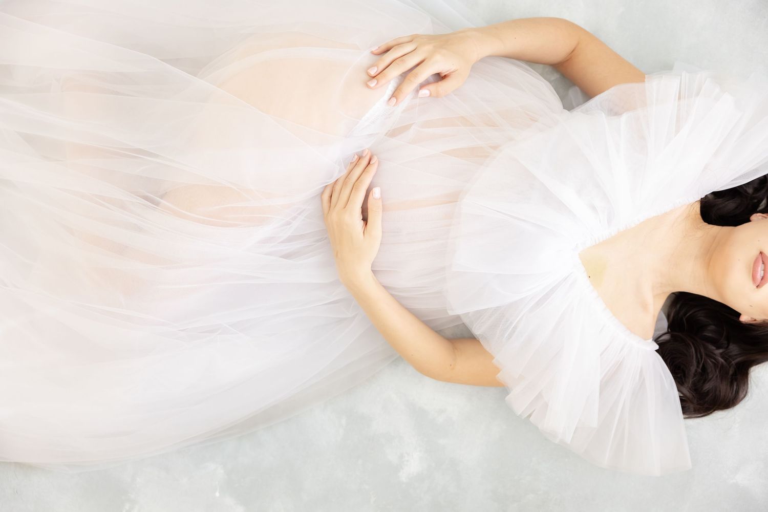 Ethereal overhead view of someone in a flowing white tulle gown lying on a light background.