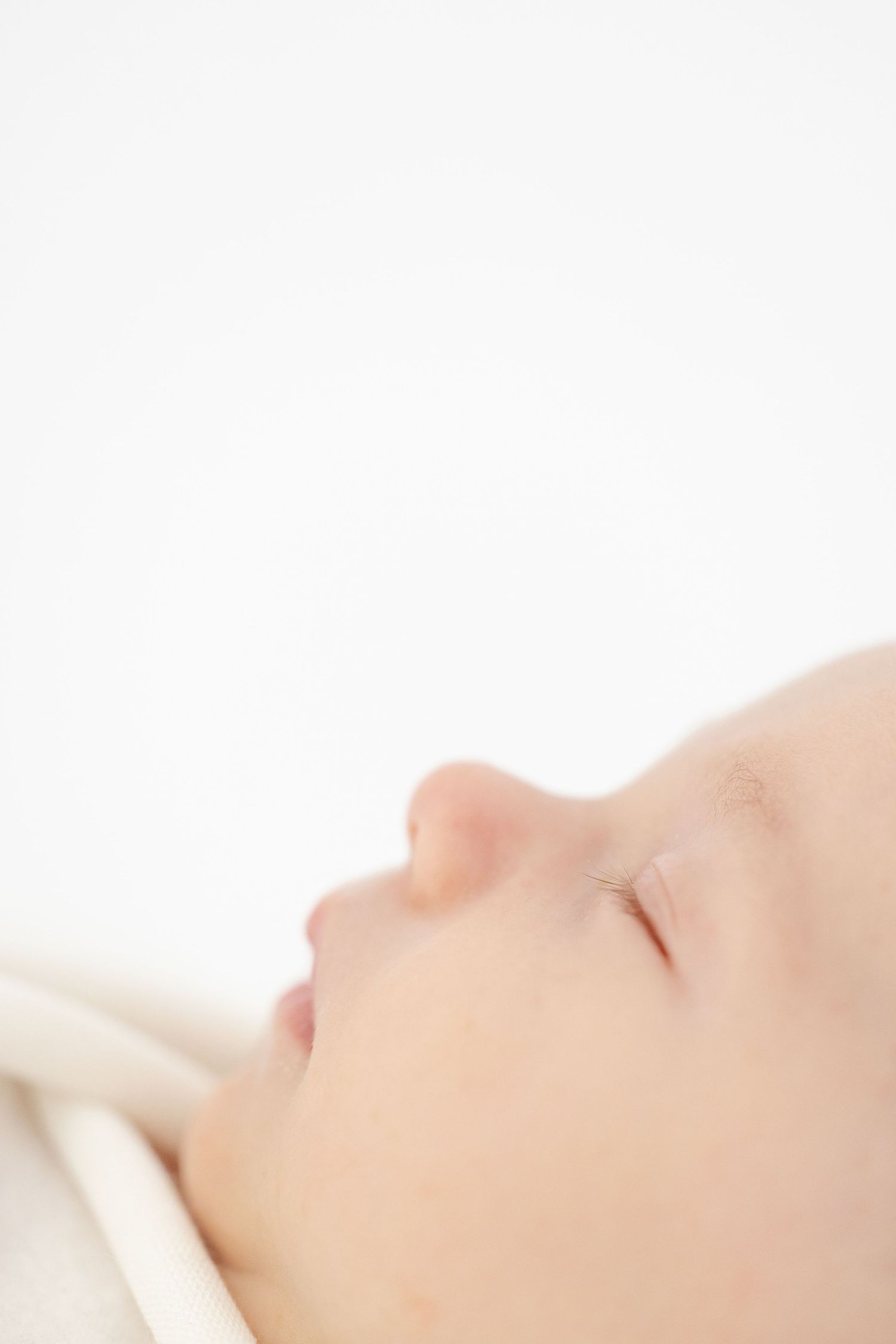 A close-up profile view of sleeping newborn on white bedding with soft lighting by Columbus, GA newborn photographer Carolina Bowers.