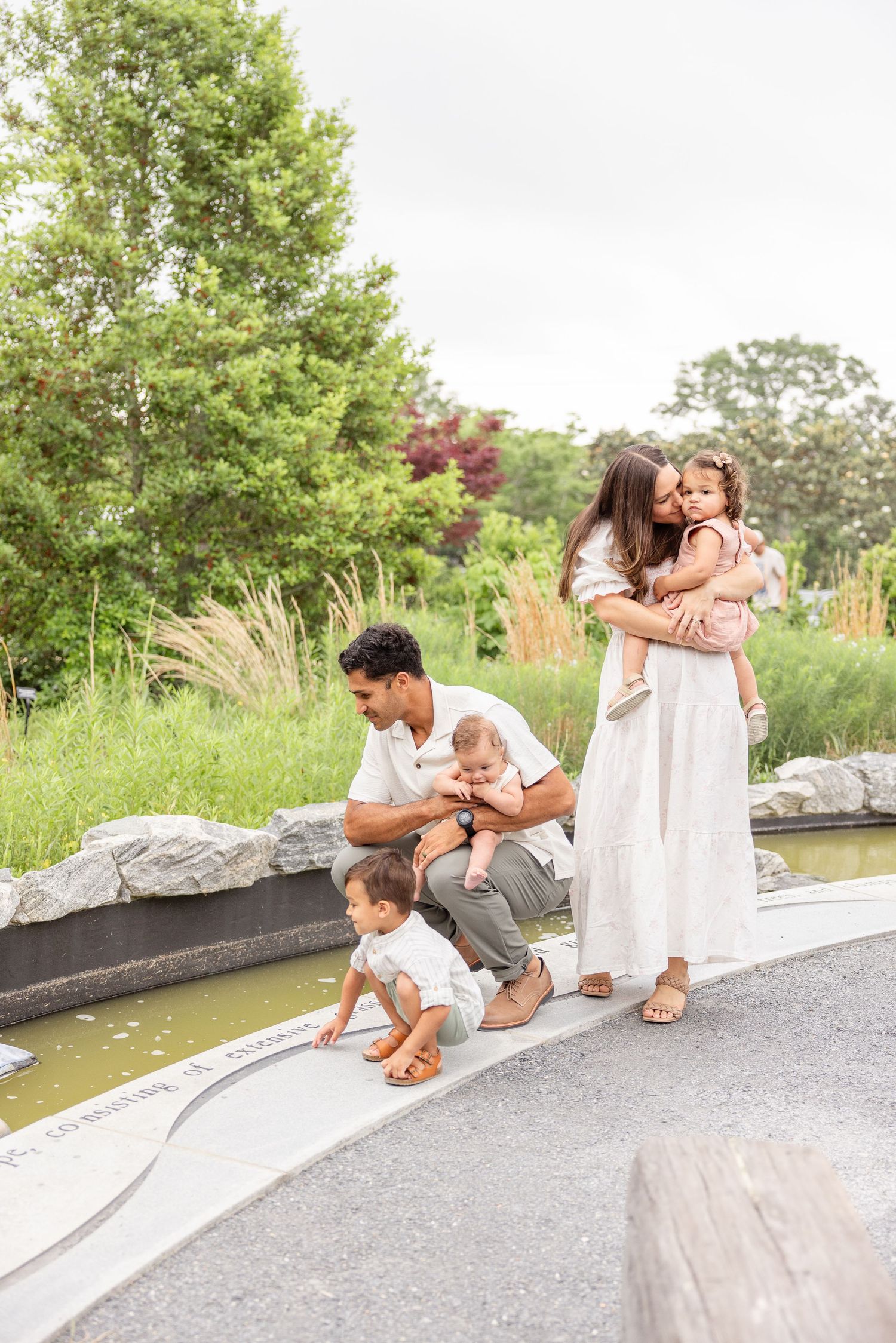 Family enjoying a peaceful moment together by a pond in a lush garden setting on a bright summer day by Columbus, GA family photographer.