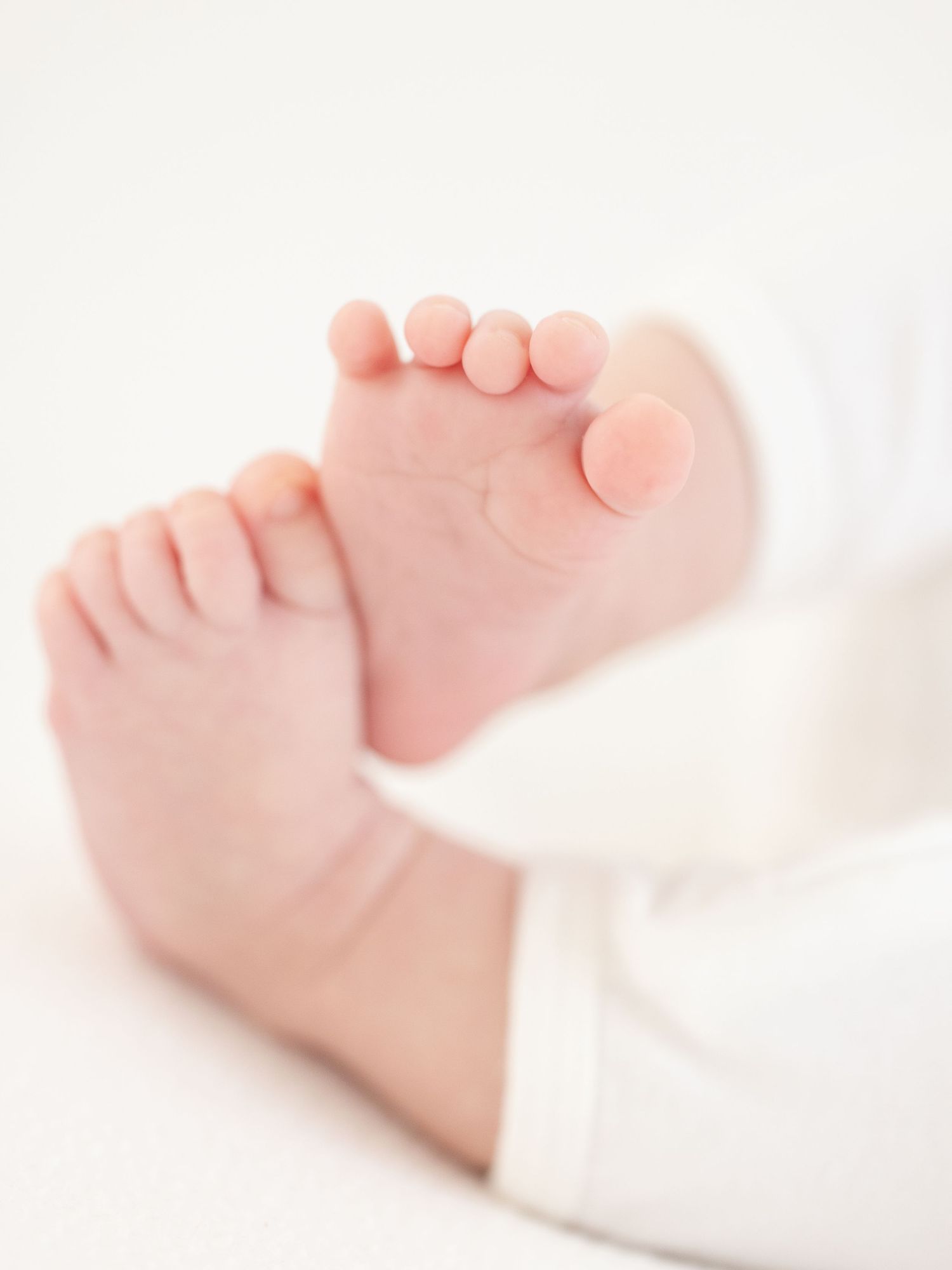 Close-up view of tiny baby feet in soft white fabric showing delicate toes and gentle curves by luxury Columbus, GA photographer.