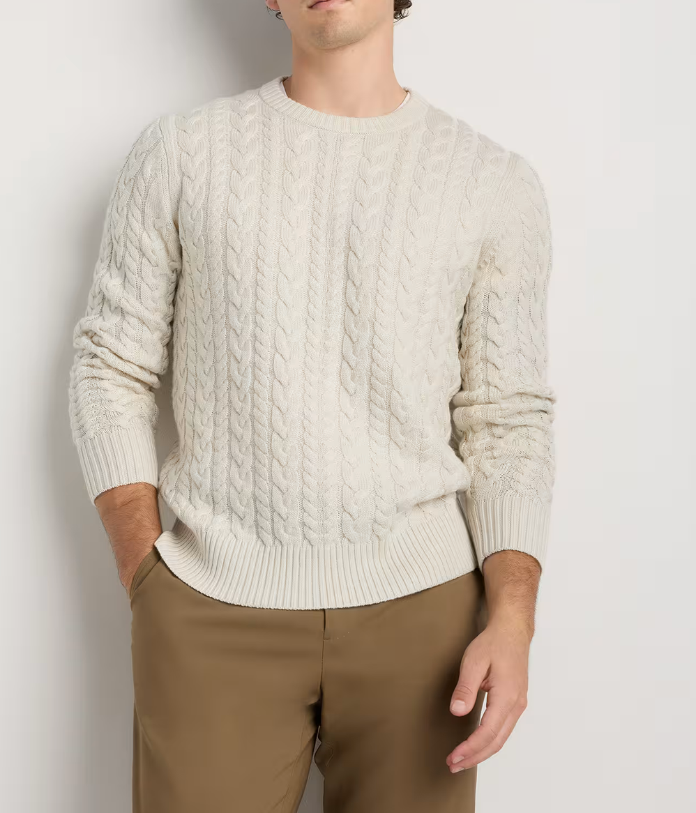 Men's cream cable-knit crewneck sweater paired with khaki pants, featuring classic braided texture.