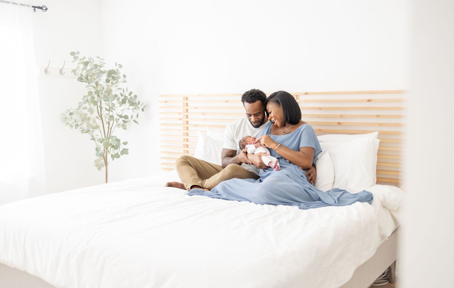 Happy Black couple sitting on bed admiring their newborn baby in a bright, modern bedroom.