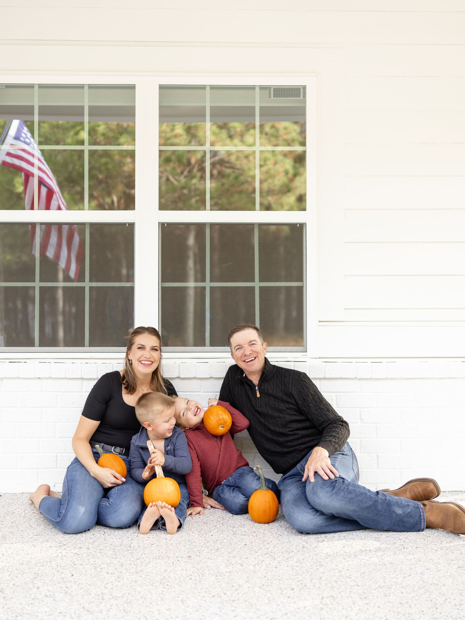 Family lounging on white porch with pumpkins in autumn wearing casual denim during their in-home family lifestyle portrait session.