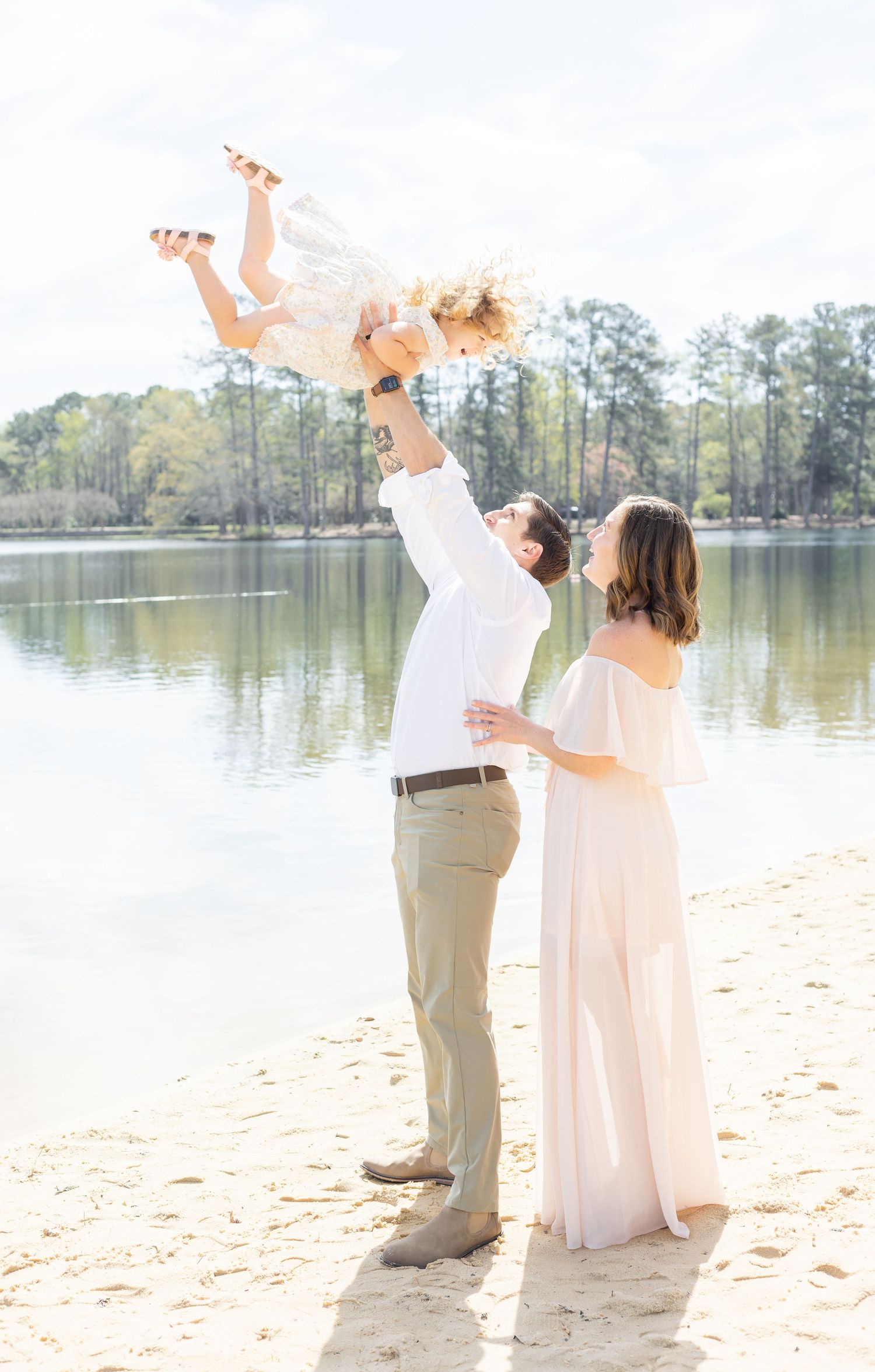 A family stands on a beach while the dad throws his daughter into the air by Columbus, GA family photographer.