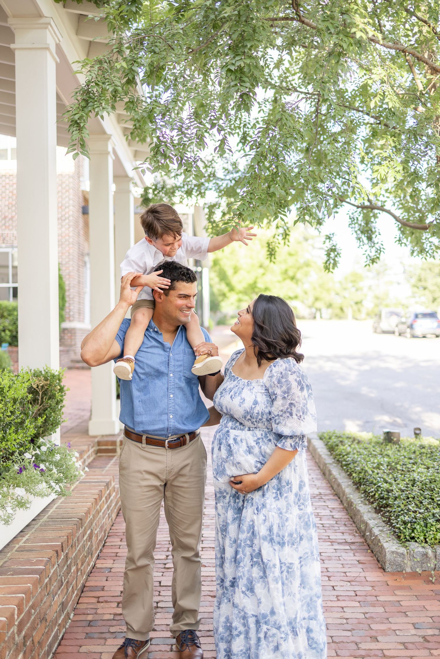 Young family enjoying a moment together on a brick path with greenery in the background at their Columbus, GA maternity session.