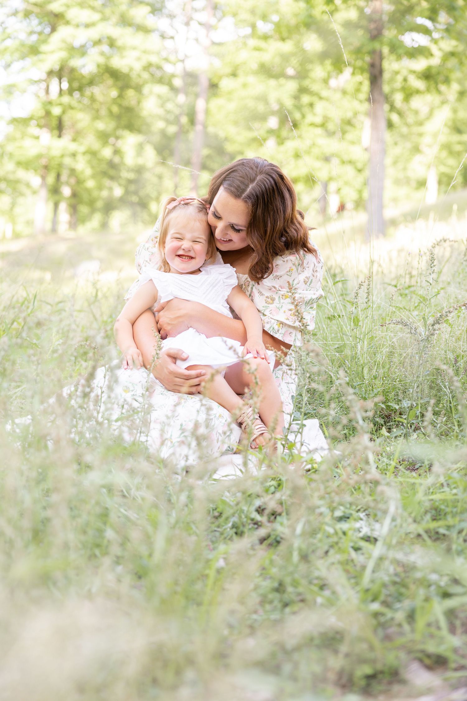 Mother and daughter share a joyful moment together while sitting in a meadow of tall grass by Columbus, GA family photographer.