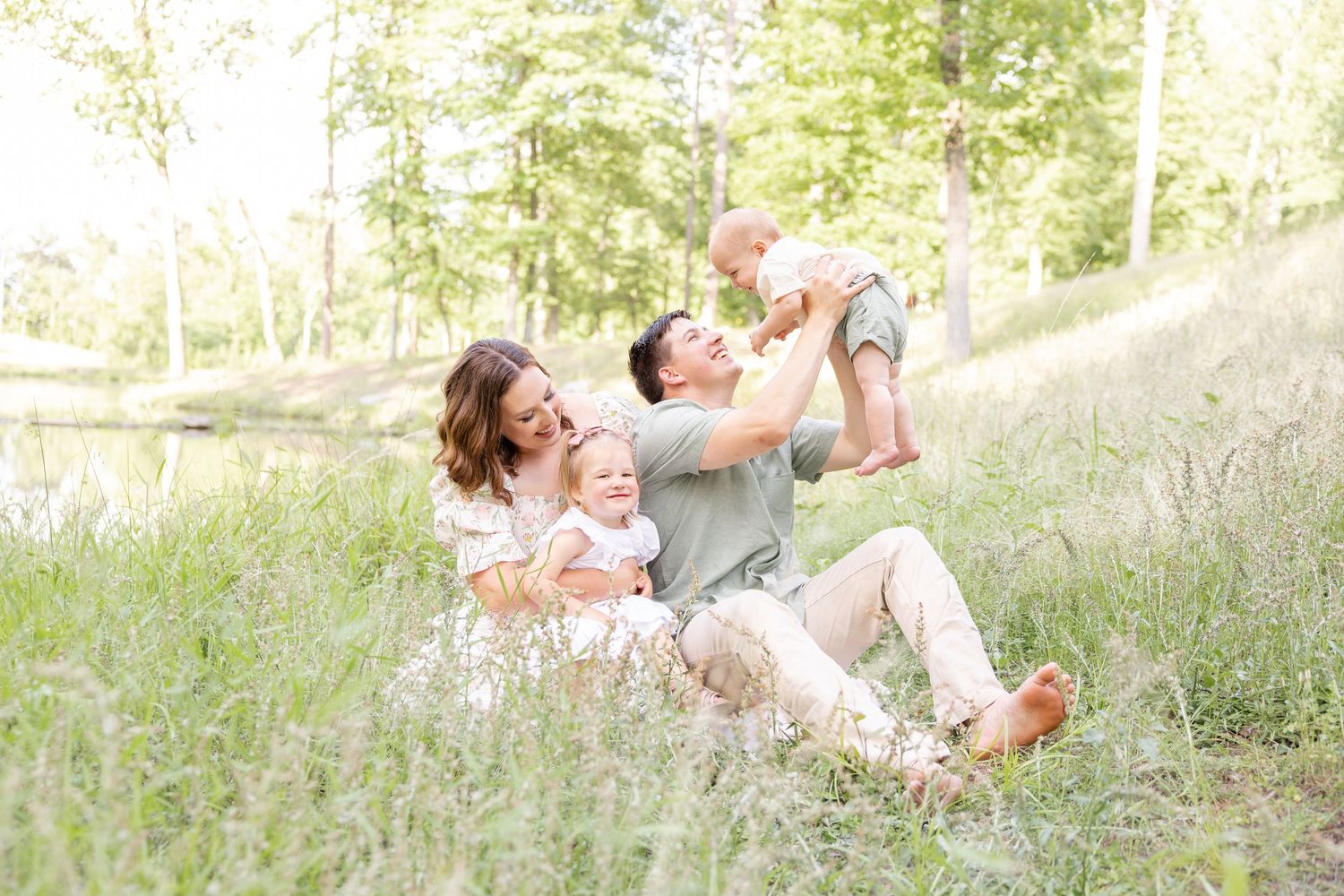 A joyful family plays together while relaxing on a grassy hillside in the sunlight at their Columbus, GA family photography session.