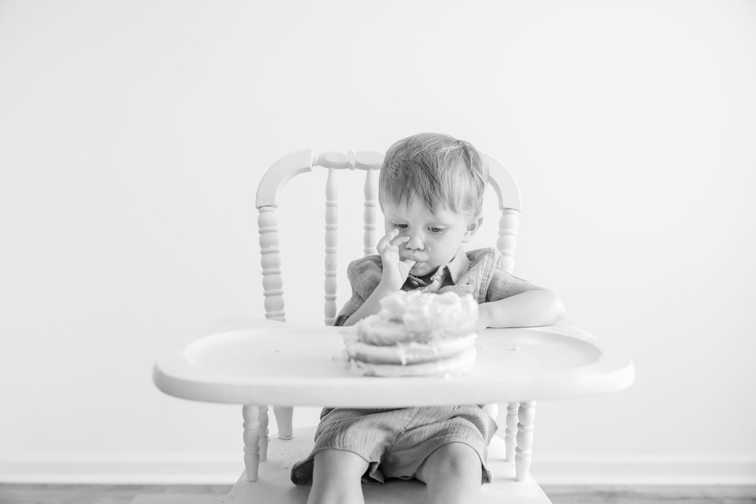 Black and white photo of a toddler boy sitting in a high chair eating birthday cake.