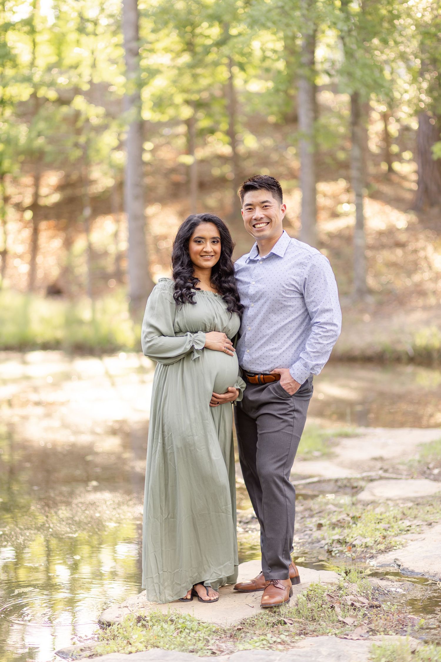 Couple poses together outdoors by a lake in a wooded area during an autumn maternity photo session in Columbus, GA.